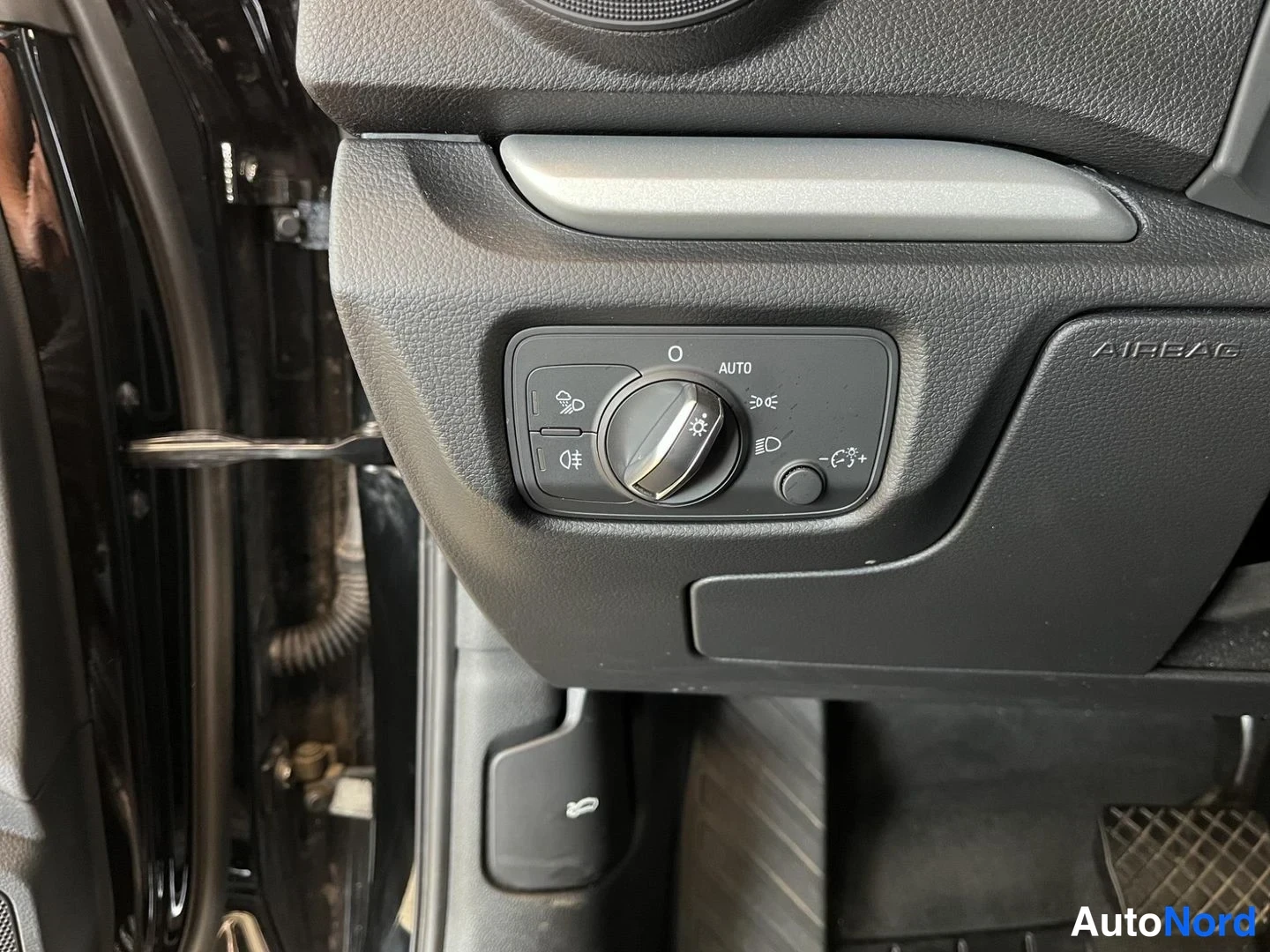 Muu: Sisätilakuva: ohjaamon valokytkinpaneeli AUTO-merinnällä ja AIRBAG-teksti kojelaudan päädyssä, tumma sisusta.