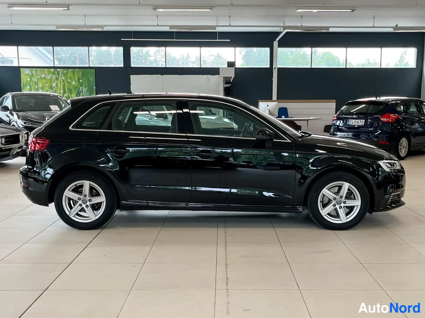Sivulta: Mustan Audi A3:n oikea sivuprofiili neljästä ovasta ja alumiinivanteista autonhallissa.