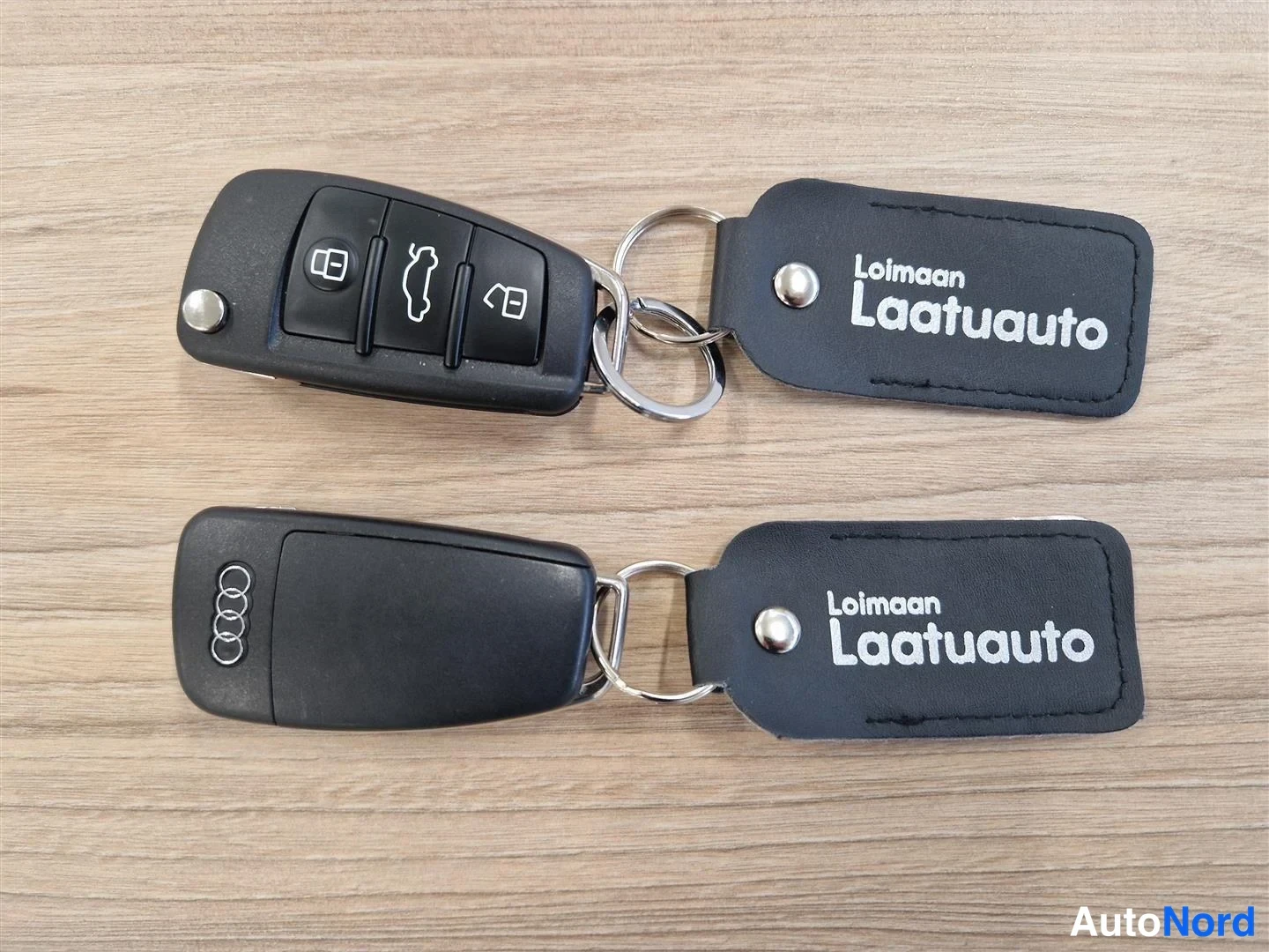Muu: Kaksi Audi-avainääntä ja kaksi Loimaan Laatuauto -avainnauhaa puupöydällä.