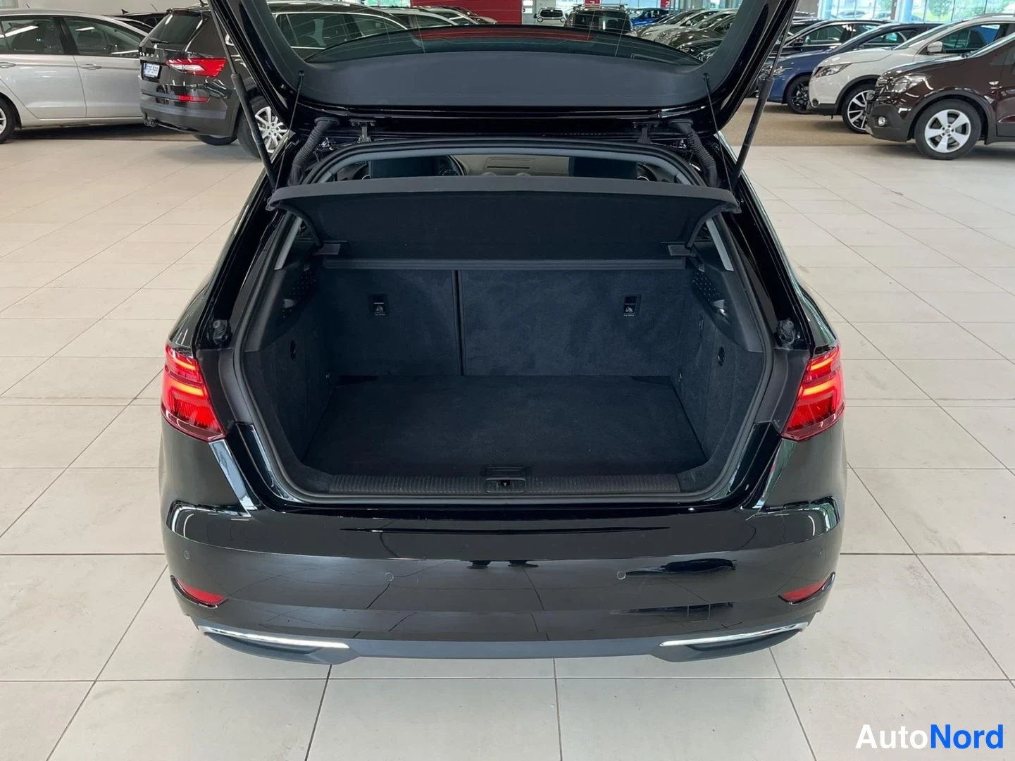 Takaa: Musta Audi A3 avoimella tavaratilällä; matot ja varusteet näkyvät tavaratilan pohjalla.