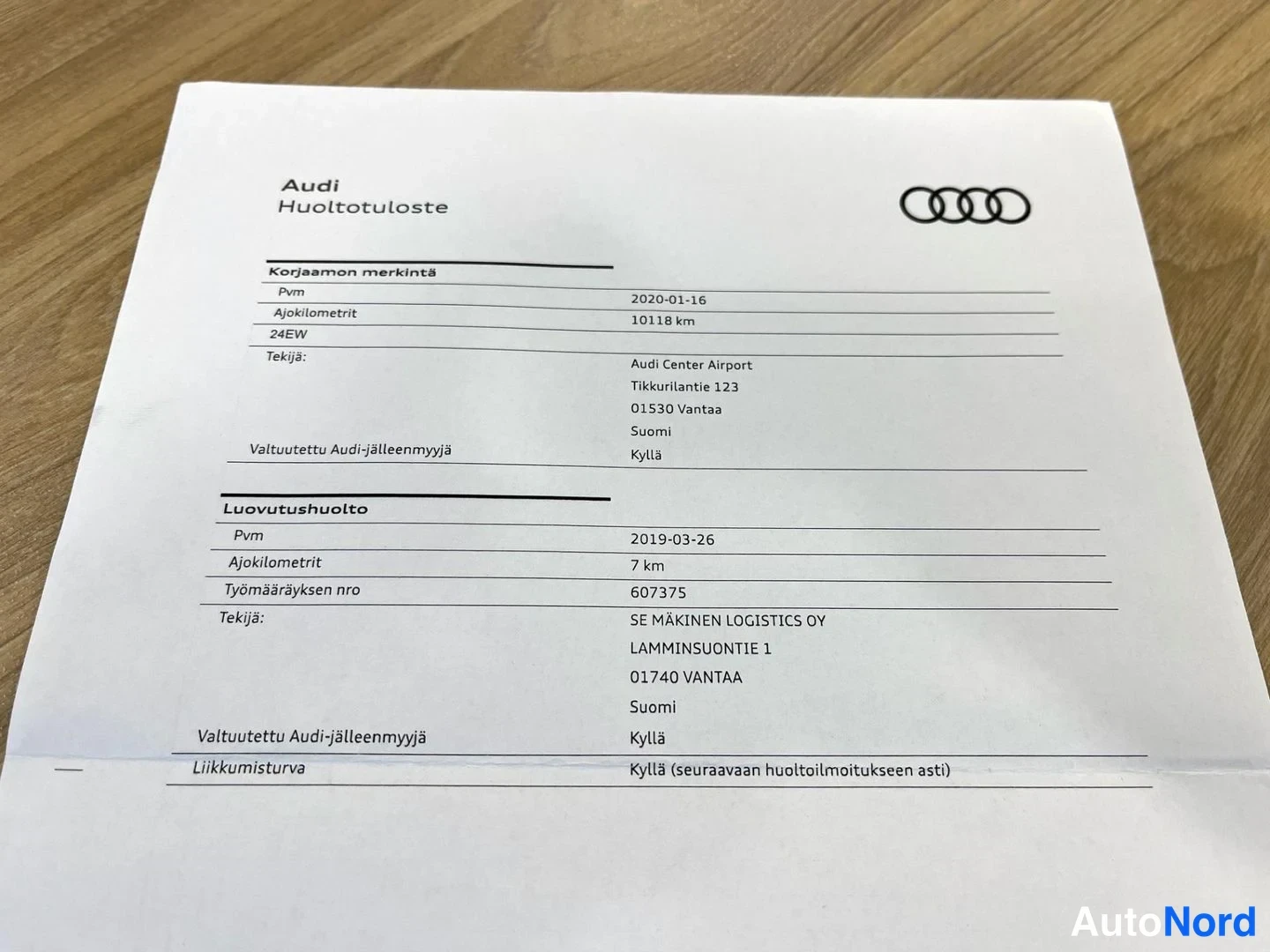 Yksityiskohta: Audi-huoltotuloste paperilla: korjaamon merkintä 2020-01-16 (10 118 km) ja luovutushuolto 2019-03-26 (7 km).