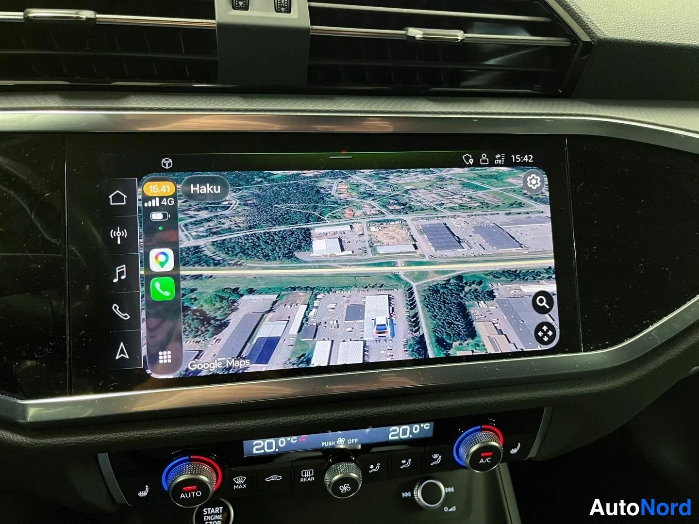 Yksityiskohta: Keskikonsolin näyttö CarPlayn kautta käytettävällä Google Maps -kartalla satelliittinäkymässä, haku-kenttä 'Haku' ylhäällä, kellonaika 15:42.
