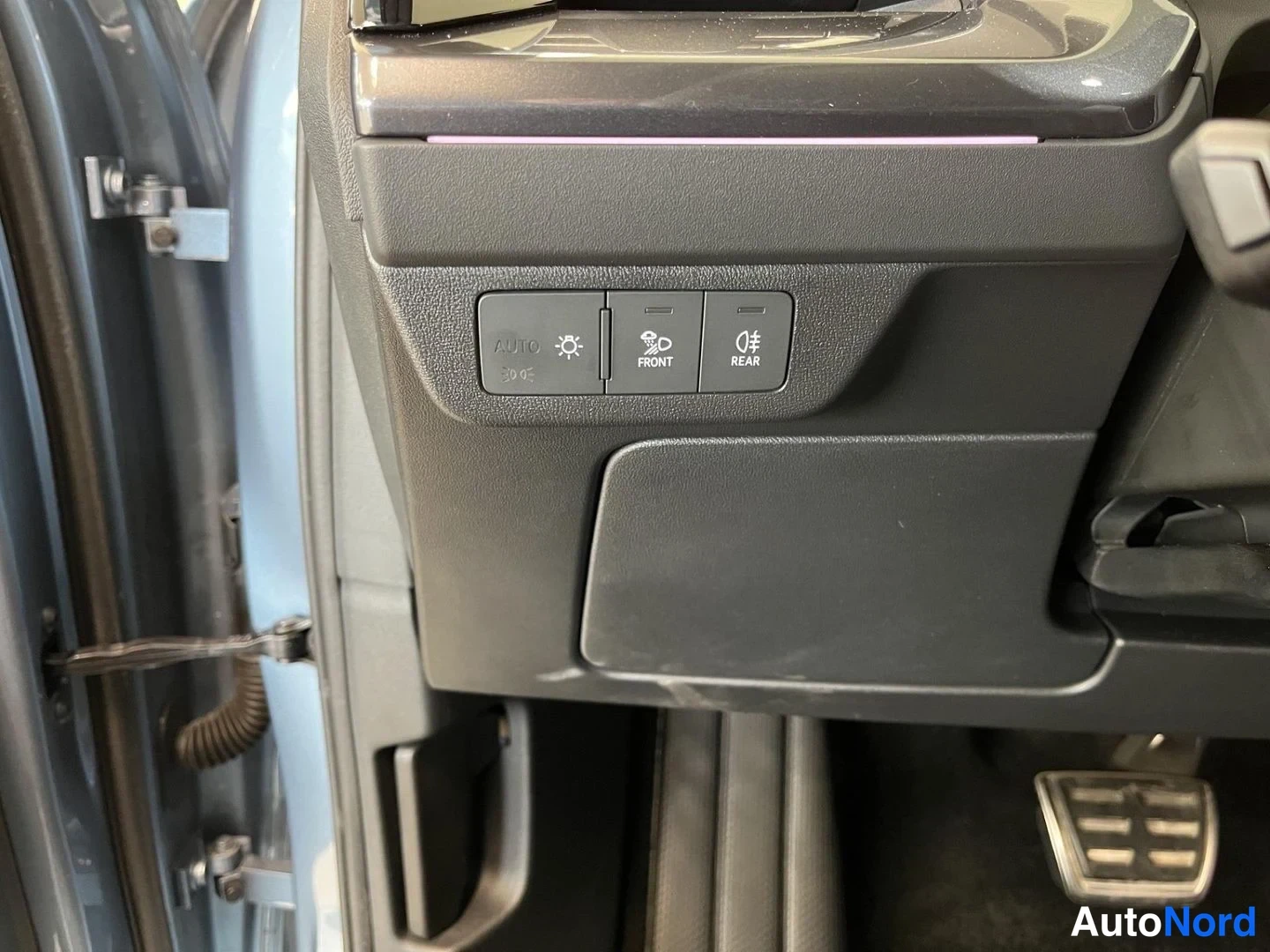 Yksityiskohta: Kojelaudan alaosan valokytkimet: AUTO-asento, etusumavalot (FRONT) ja takasumavalot (REAR) tummalla paneelilla; ovenraja ja tuulilasinpesurin suutin näkyvät vas