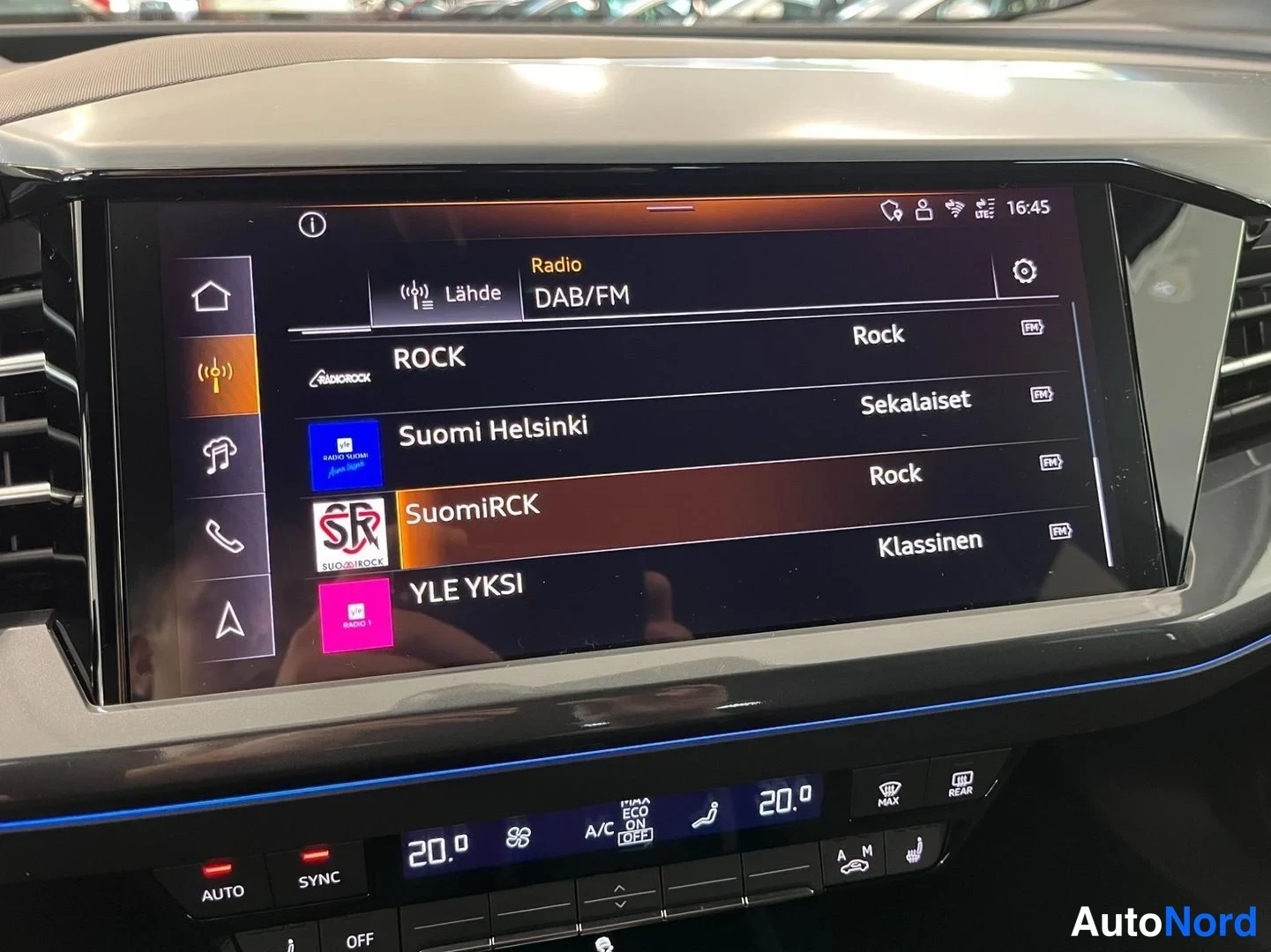 Yksityiskohta: Sisätilakuva: Audi'n tietoviihdejärjestelmän näyttö radiotoiminnossa (DAB/FM), jolla näkyvät kanavat ROCK, Suomi Helsinki, SuomiRCK ja YLE YKSI.
