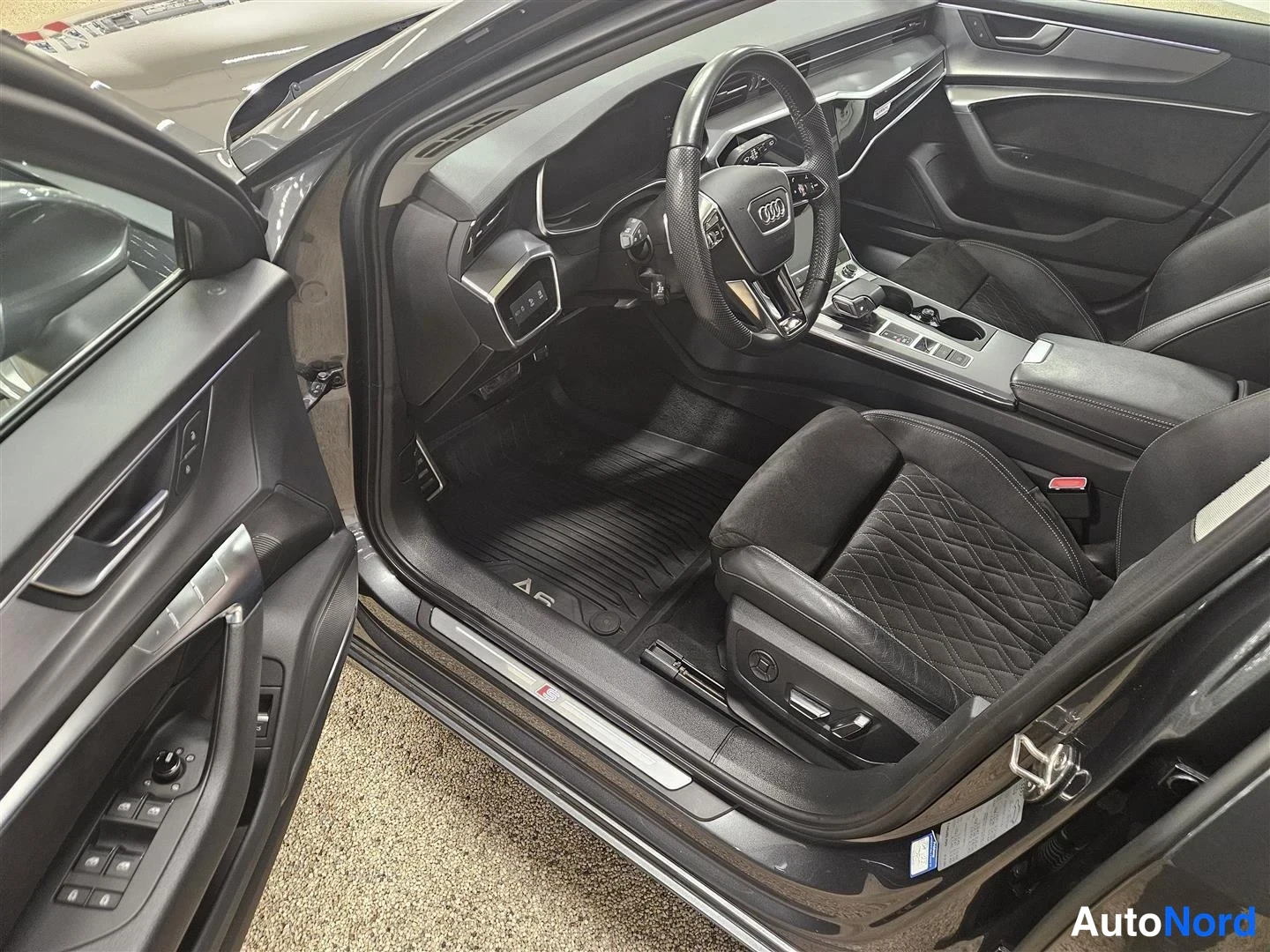 Muu: Auton sisätila: Audi-ohjauspyörä, quilted istuin, mittaristo ja A6-lattiamatto näkyvät avatun kuljettajanoven läpi.