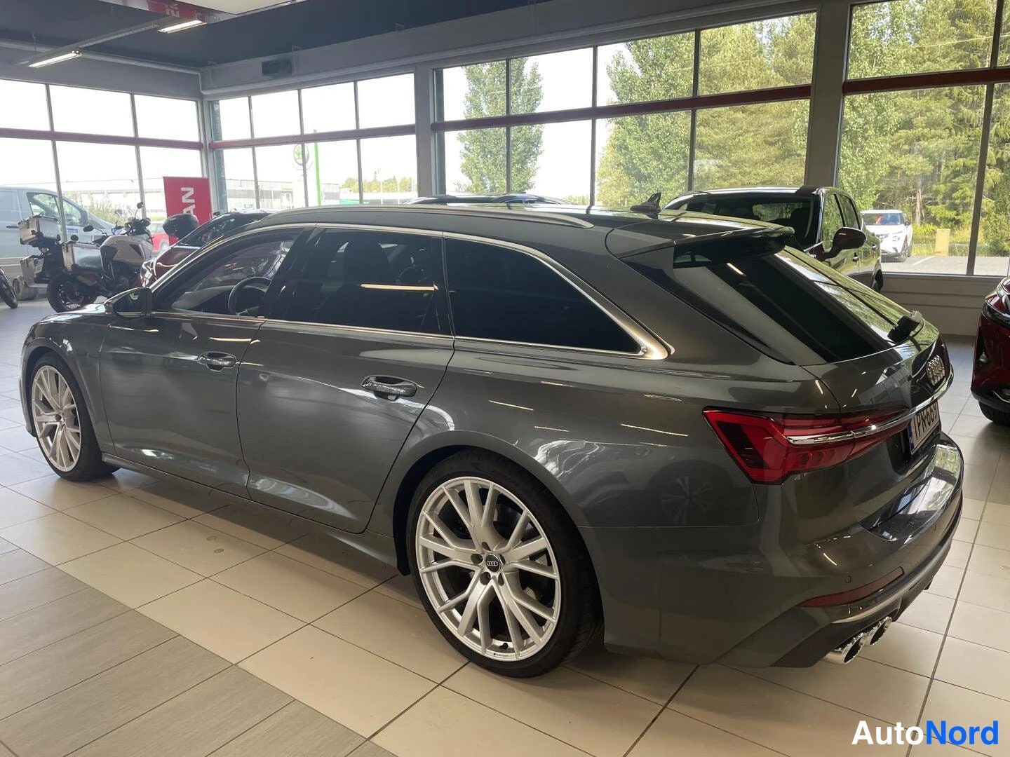 Takaviisto: Audi S6 Avant -farmari autokaupan näyttelytilassa, takalysy vasemmalla, tummanharmaa maalaus.