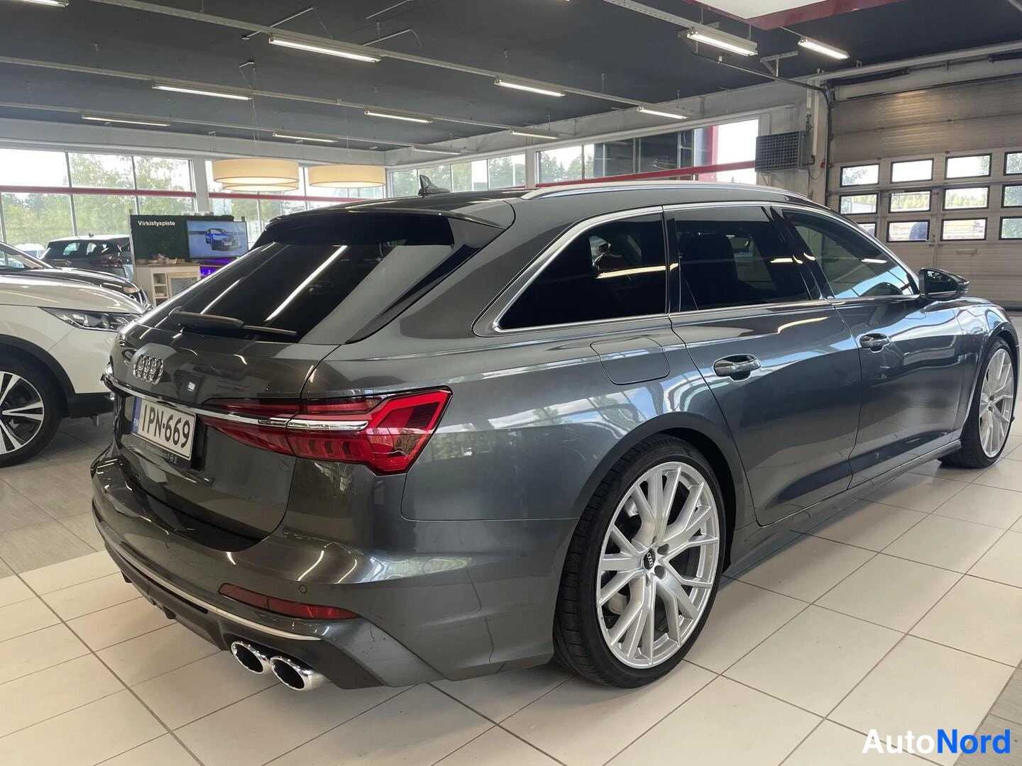 Takaviisto: Audi S6 Avant -farmari autokaupan näyttelytilassa, takalysy vasemmalla, tummanharmaa maalaus.