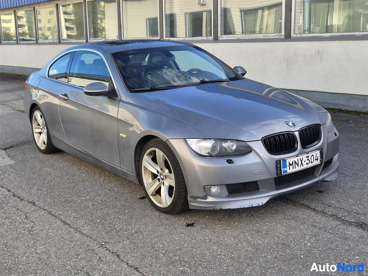Etuviisto, nokka oikealle: BMW-coupé kolmella neljännestä kulmasta keula oikealla, harmaa kori, rekisterikilpi.