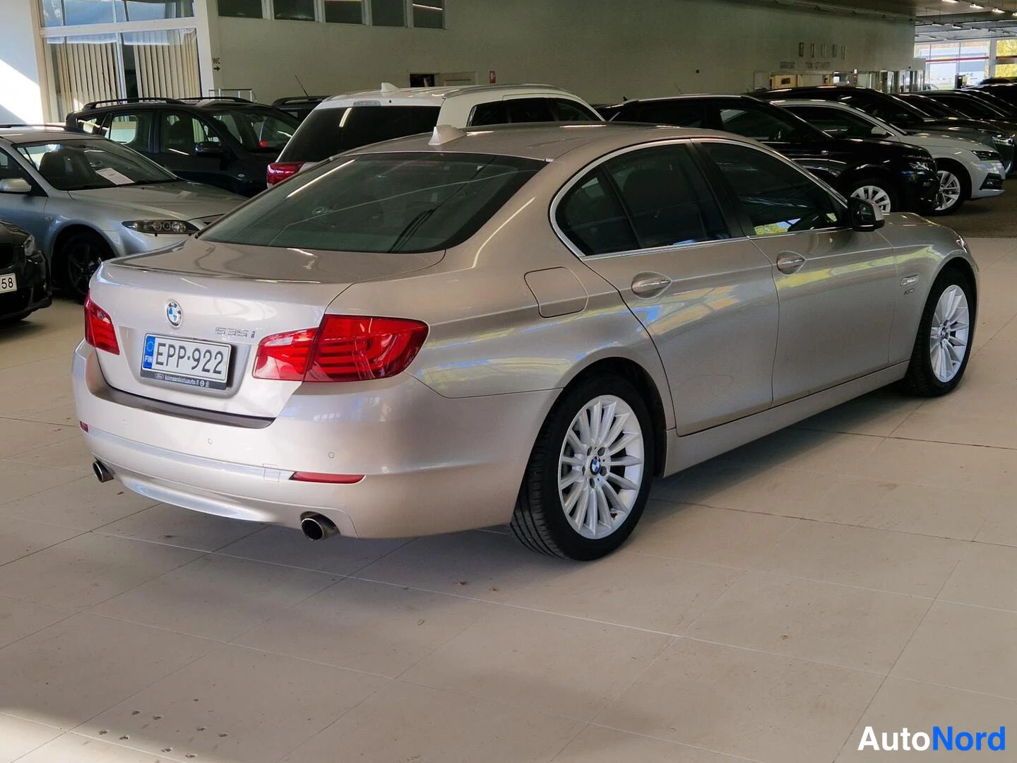 Takaviisto: Kultainen BMW 535i sedanan takakulmakuva sisätiloissa, rekisterikilpi ja kolmihuulinen pakoputki.