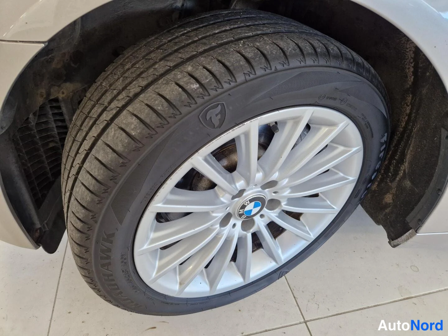 Yksityiskohta: BMW-merkkinen hopeisen monipuolainen vanteen rengas Firehawk-sivuseinällä, lähikuva pyörästä.
