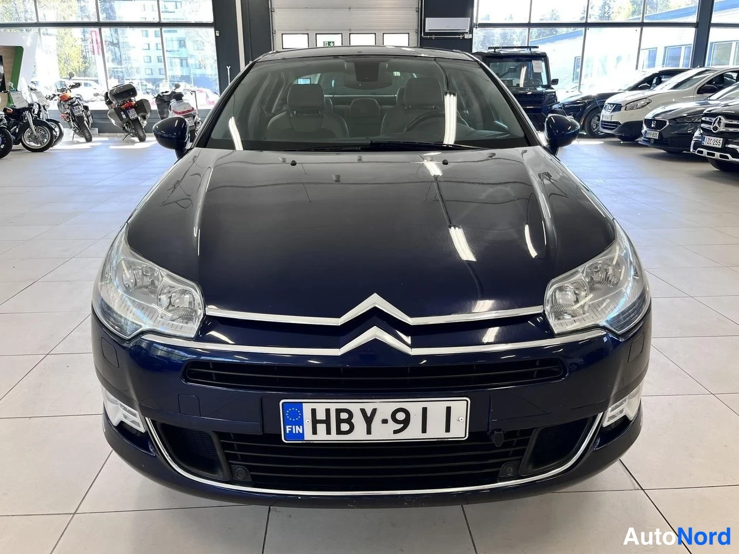 Edestä: Tummansinisen Citroën C5:n keula suoraan edestäpäin; rekisterikilpi, Citroënin tunnus konepellissä ja sumuvalot puskurissa.