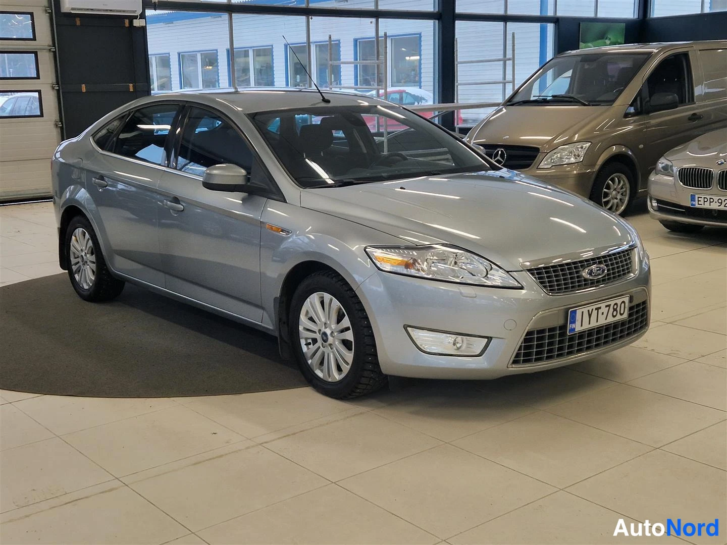 Etuviisto, nokka oikealle: Hopeanvärinen Ford Mondeo -henkilöauto autonäyttelytilassa, etukulmanäkymä oikealta; rekisteritunnus.