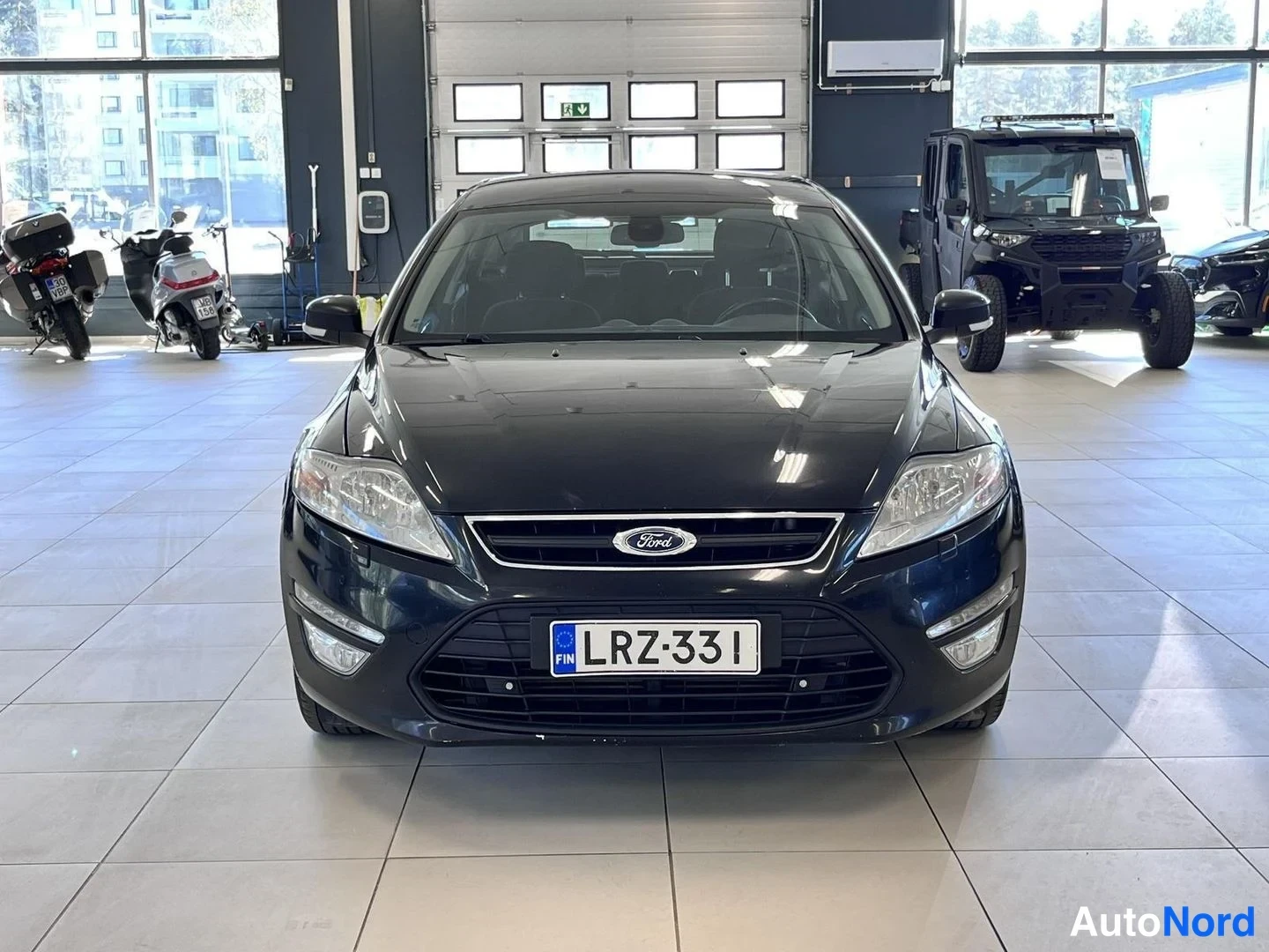 Edestä: Mustan Ford Mondeon suora etunäkymä myyntihallissa, rekisteritunnus.