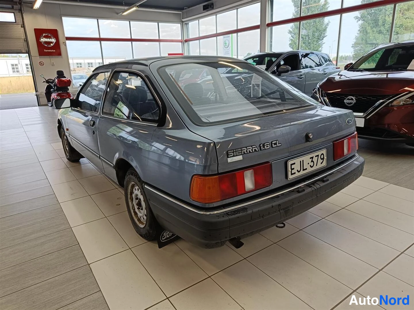 Takaviisto: Harmaa kolmiovinen hatchback auto takaviistöstä, peräluukussa SIERRA 1.8 CL -teksti ja rekisterikilpi.
