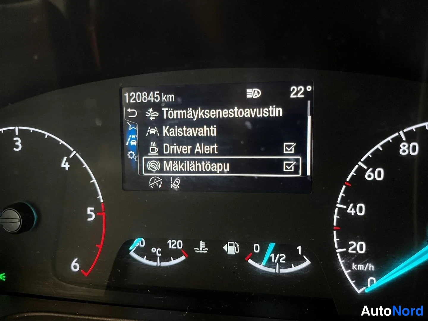 Yksityiskohta: Kojetason mittaristo: matkamittari näyttää 120845 km, ruudulla tekstit Törmäyksenestoavustin, Kaistavahti, Driver Alert ja Mäkilähtöapu.