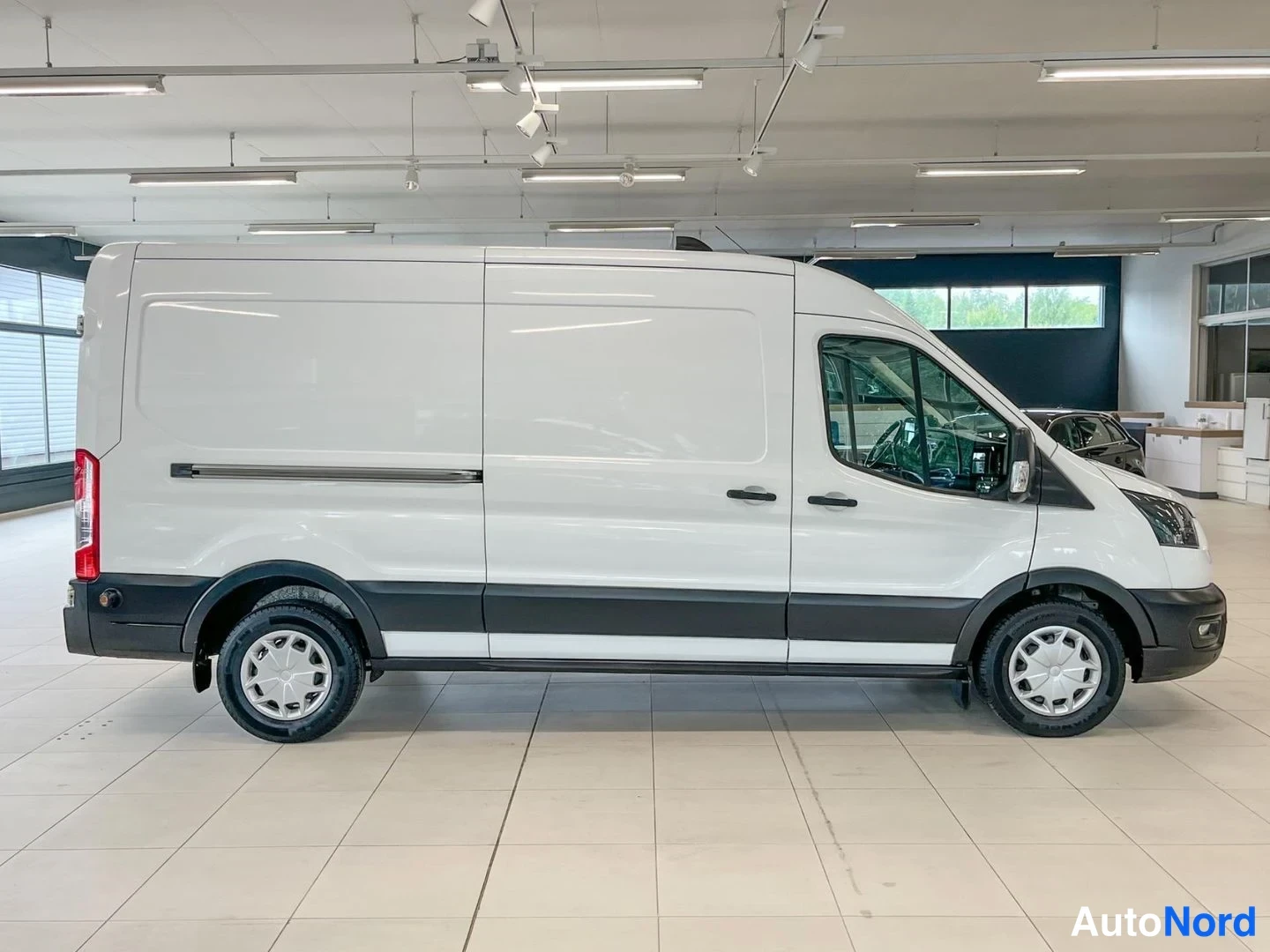 Etuviisto, nokka oikealle: Ford Transit -pakettiauton sivuprofiili; valkoinen korii, takana jakokori ja kaksi liukuovea, tummat puskurilistat, kevytmetallivanteet.