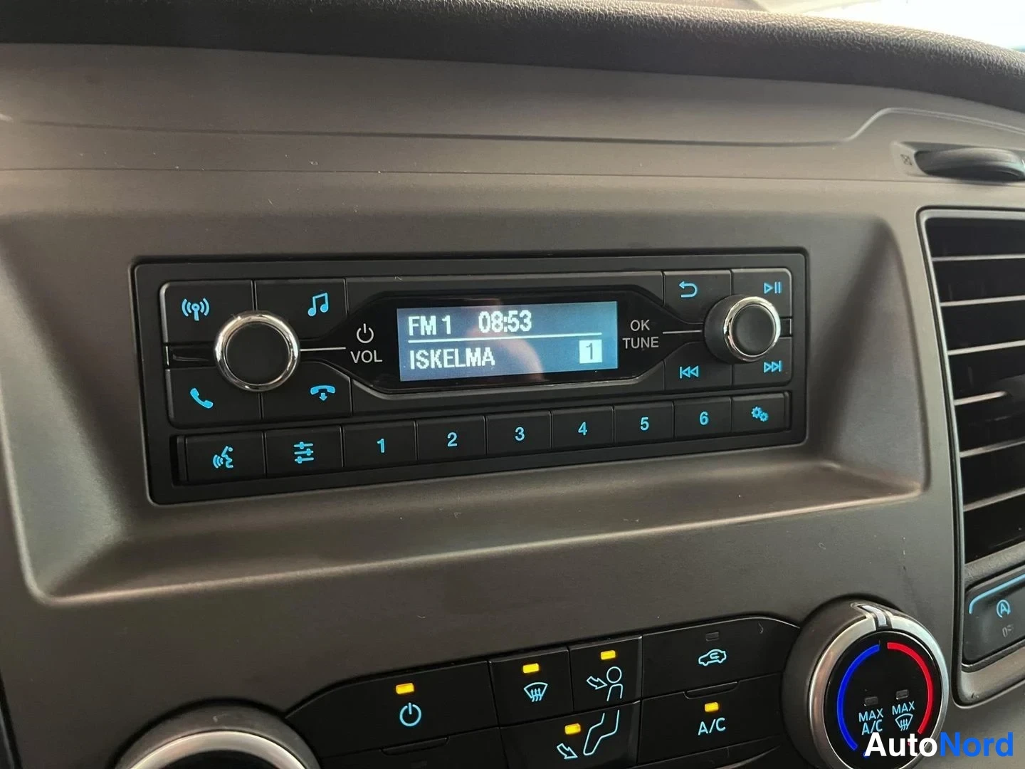 Yksityiskohta: Radio näytöllä FM 1 ISKELMA, kellon aika 08:53, ilmastointipainikkeet A/C ja MAX A/C