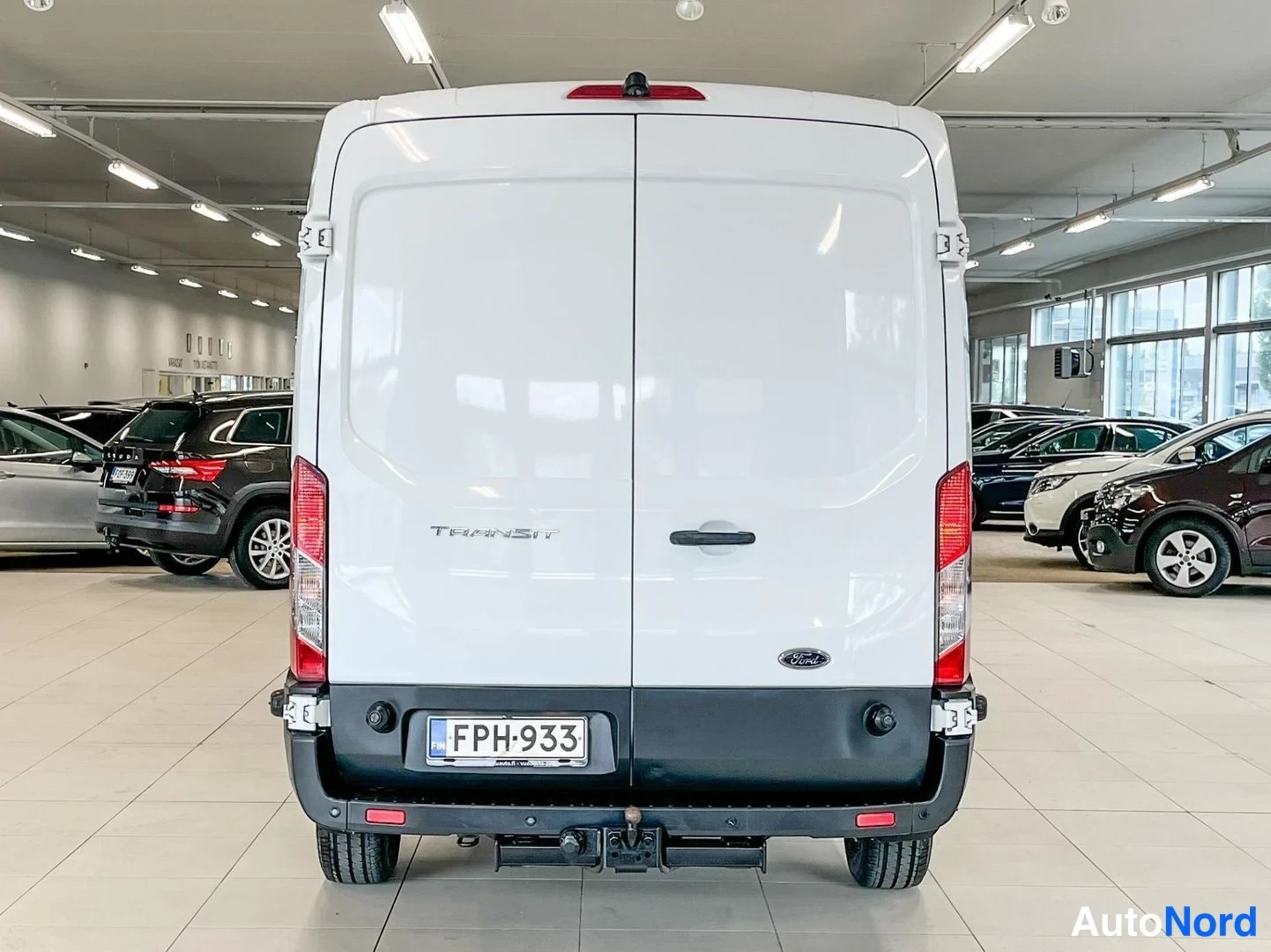Takaa: Ford Transit -pakettiauton takaosa takaa kuvattuna, valkoinen koripelti, TRANSIT-teksti ovessa, rekisterikilpi ja kuormakoukku.