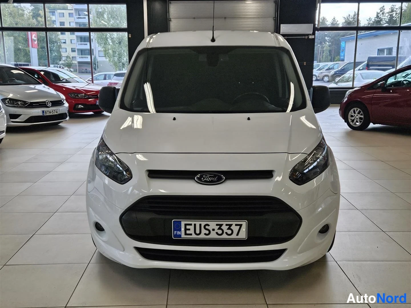 Edestä: Valkoinen Ford Transit Connect suoraan edestä päin, Ford-merkki ja rekisteritunnus näkyvissä.
