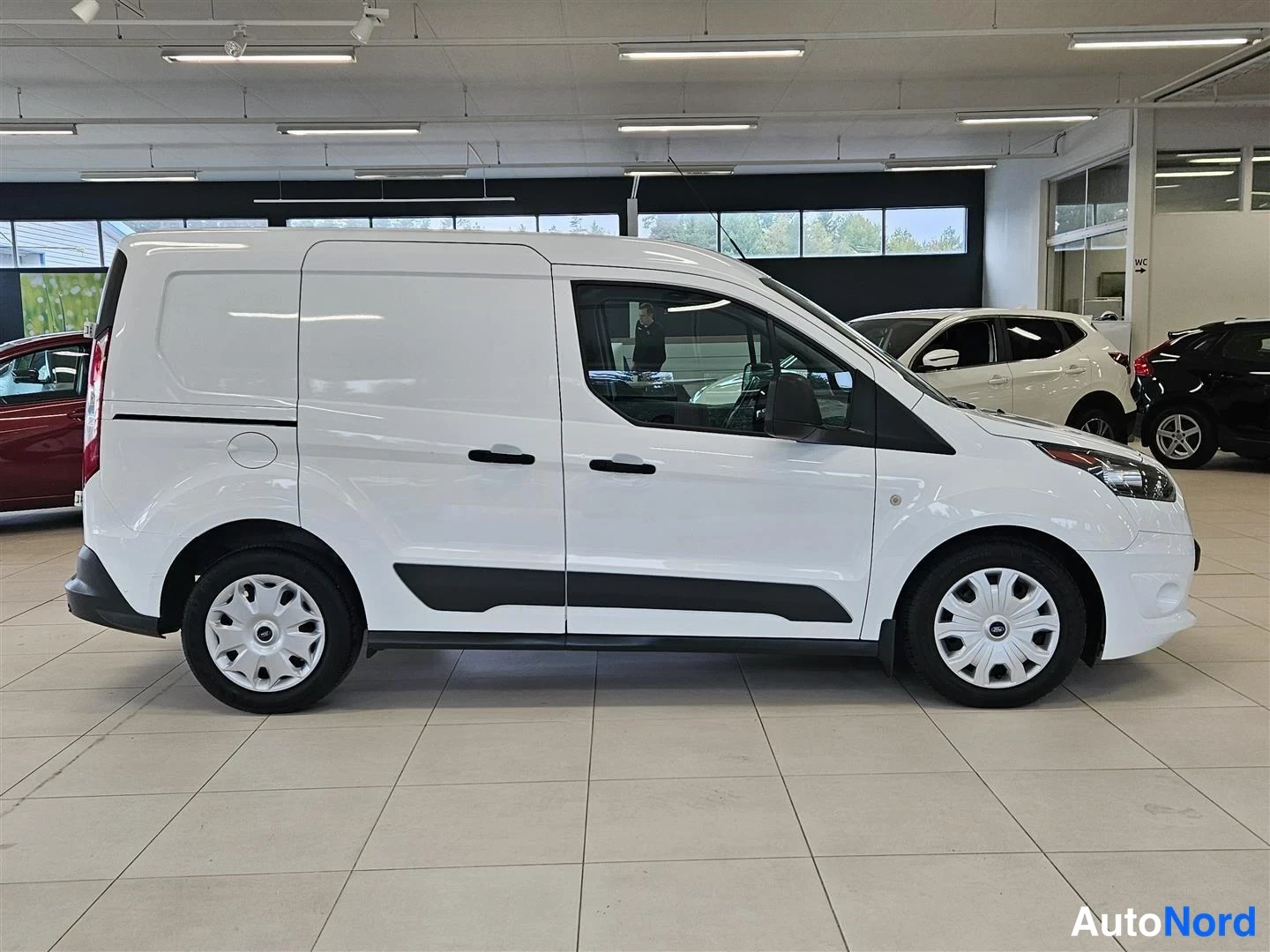 Sivulta: Valkoinen Ford Transit Connect -pakettiauto sivulta nähtynä autonhallin lattiassa.