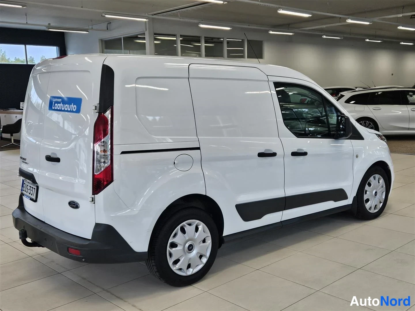 Takaviisto: Ford Transit Connect -pakettiauton takakolmasosa ja sivu valkoisena autosalissa; rekisterikilpi ja sininen Laatuauto-tarra takaluukussa.