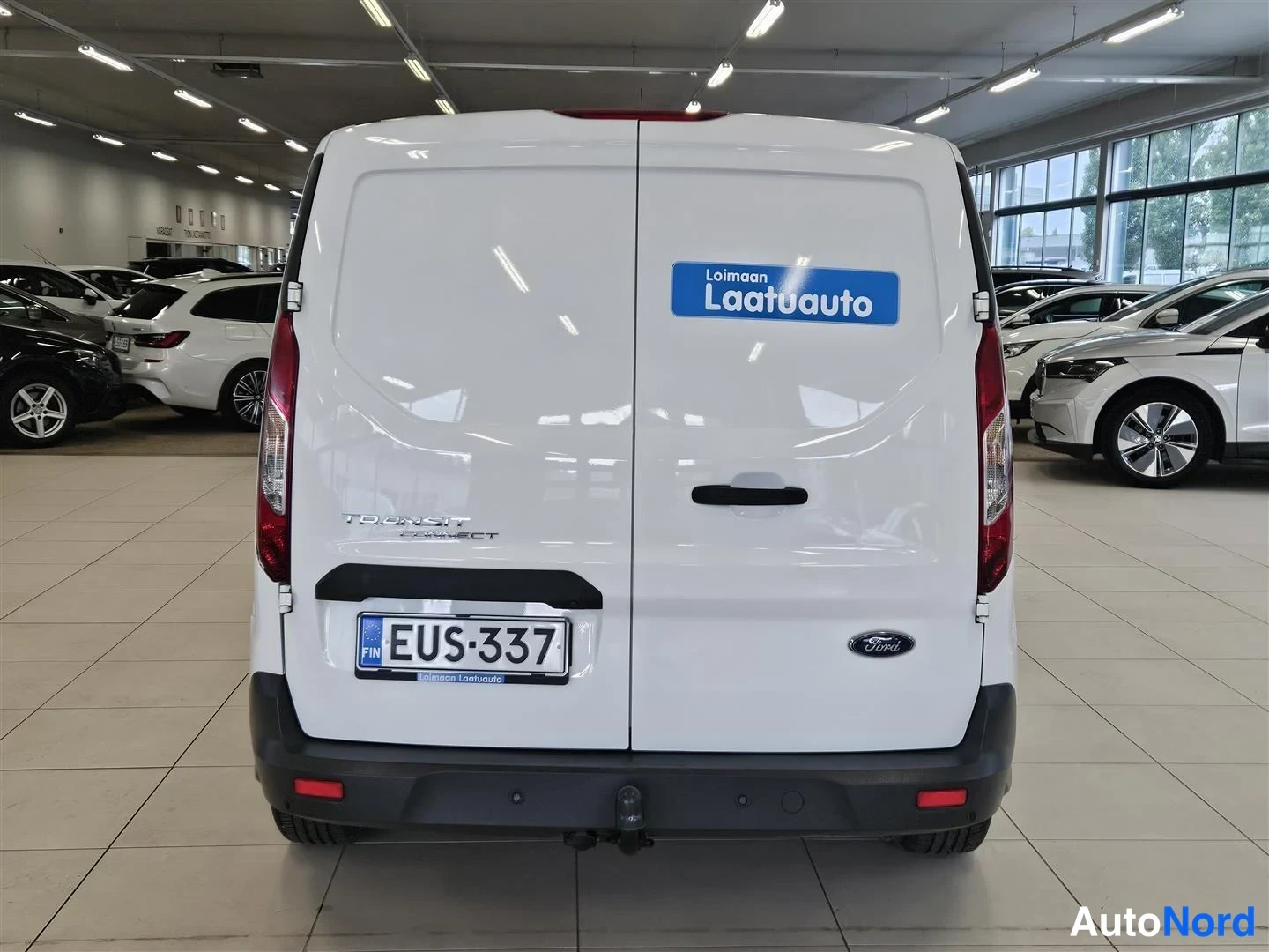 Takaa: Valkoisen Ford Transit Connect -pakettiauton takaosa suoraan takaa, rekisterikilpi ja sininen Loimaan Laatuauto -tarra takaluukussa.