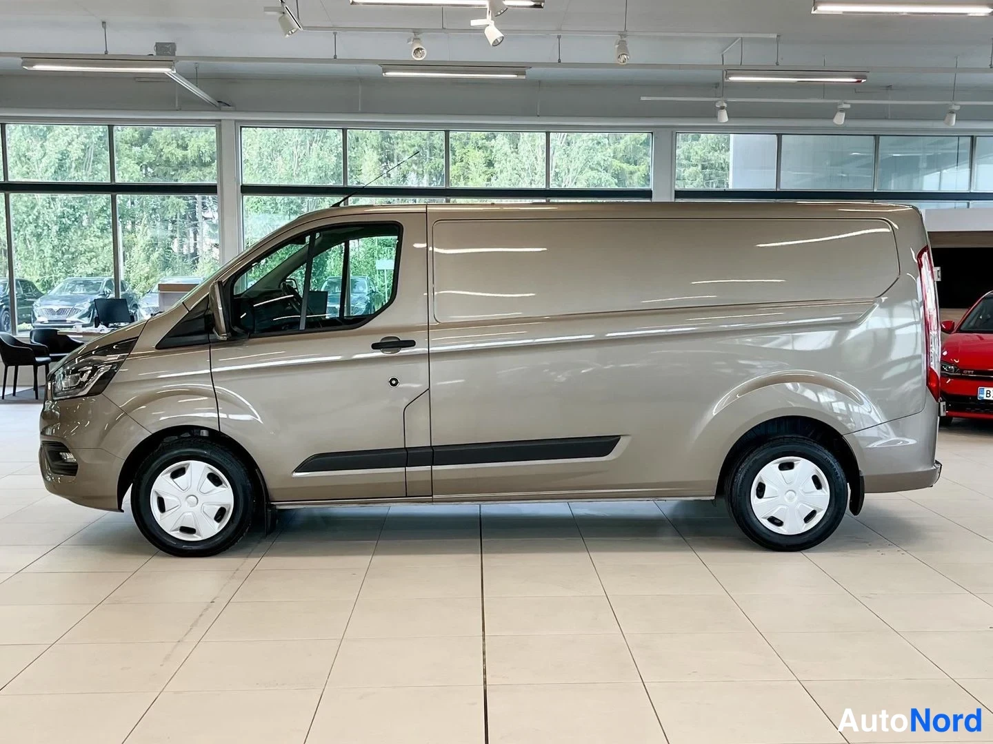 Sivulta: Ford Transit Custom -pakettiauto sivulta, vaaleanruskea maali. Auton vasen sivu näkyy kokonaan.