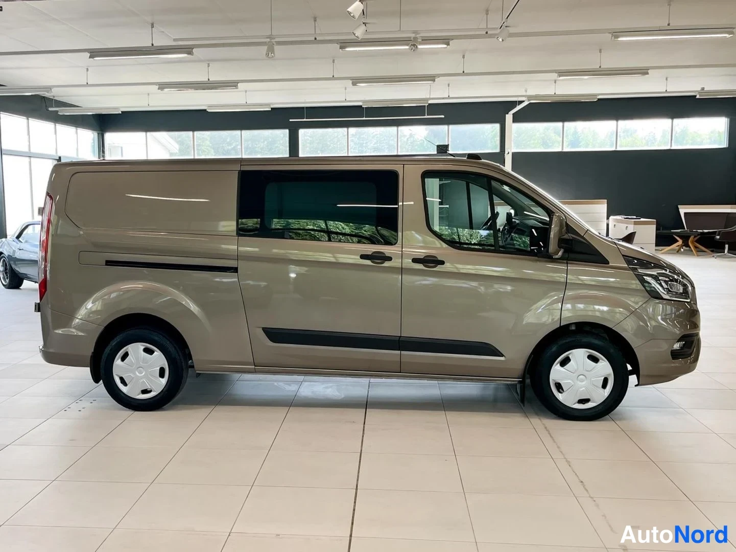 Etuviisto, nokka oikealle: Ford Transit Custom -pakettiauto sivulta oikealta, konepelti ja keula oikealla. Auton oikea sivu ja keulan osa näkyvät.