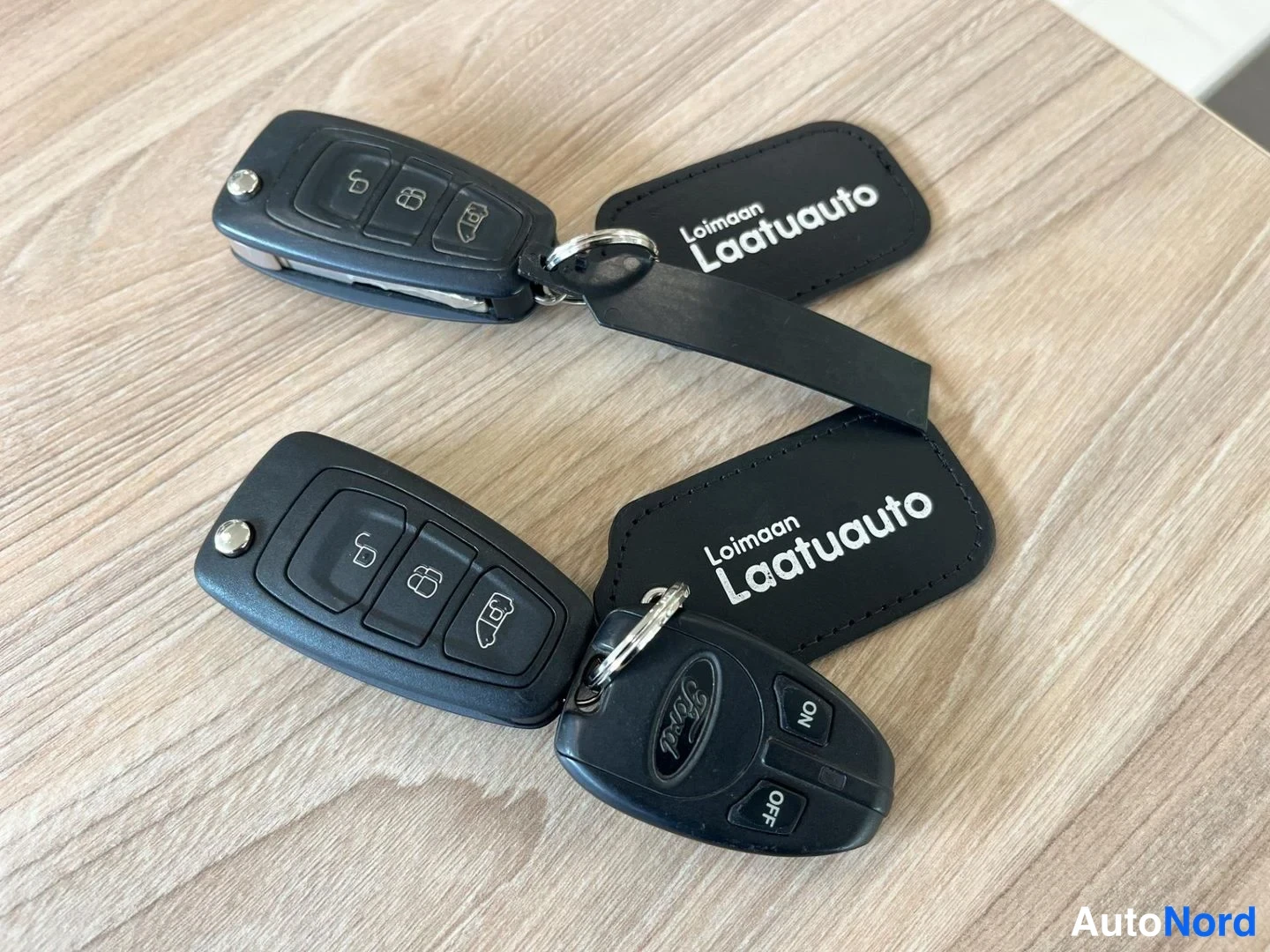 Yksityiskohta: Kaksi Ford-etäavainparia ja Loimaan Laatuauto-avainnauha puupöydällä.