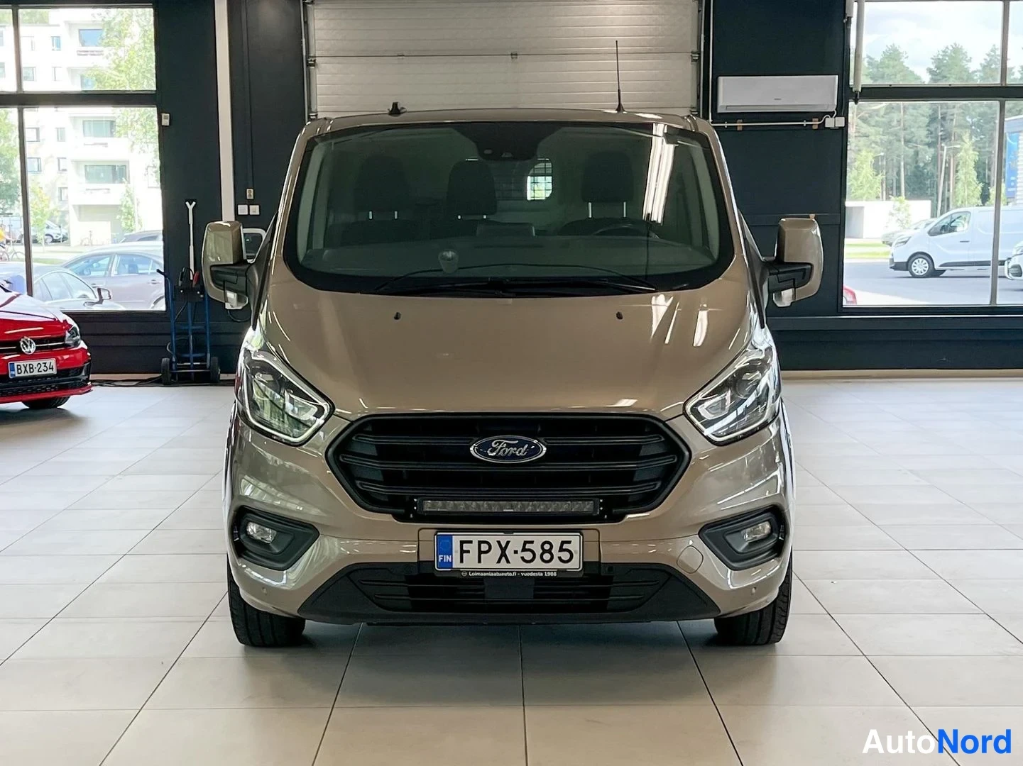 Edestä: Ford Transit Custom -pakettiauto suoraan edestäpäin, rekisterikilpi. Auton keula näkyy keskitetysti.