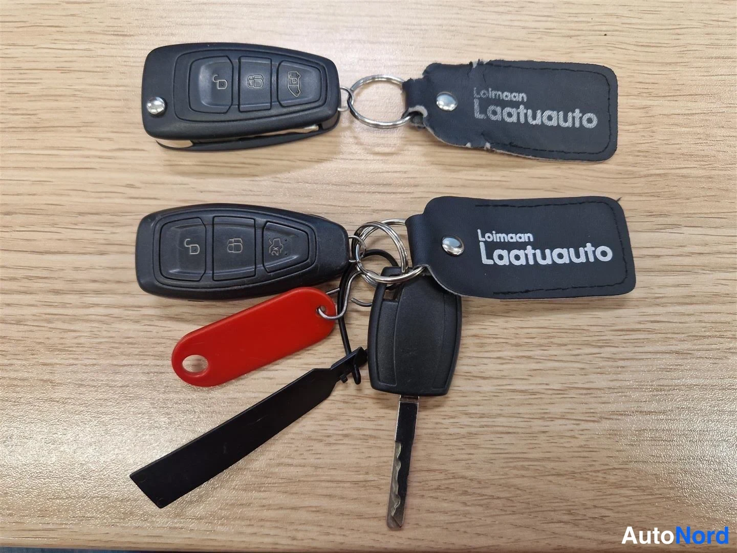Muu: Kaksi auton kauko-ohjainavainta kolmella painikkeella, täytekavain ja Loimaan Laatuauto -avainnapukkei puinen pöytä.