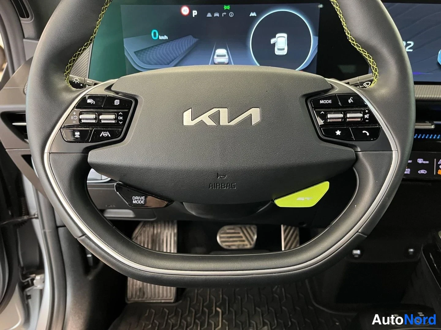 Muu: Lähikuva Kia-ohjauspyörästä, AIRBAG-teksti ja DRIVE MODE-kytkin näkyvät, takana digitaalinen mittaristo.