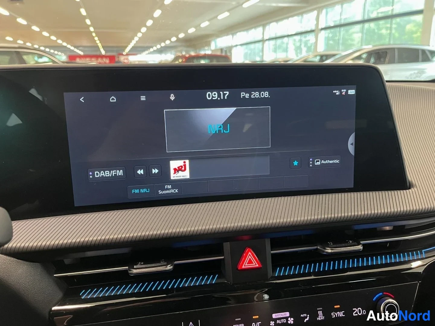 Yksityiskohta: Infotainment-näyttö soittaa NRJ-radiokanavaa DAB/FM:llä; kellonaika 09.17, päivämäärä Pe 28.08. Näytön alapuolella ilmastointipaneeli näkyy SYLK 20.0 ja SYNC-as