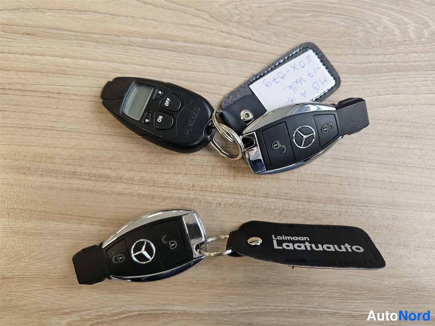 Muu: Kaksi Mercedes-Benzin kauko-ohjainavainta ja rekkastunniste merkkilapuilla vaaleanpuisen pöytätason päällä.