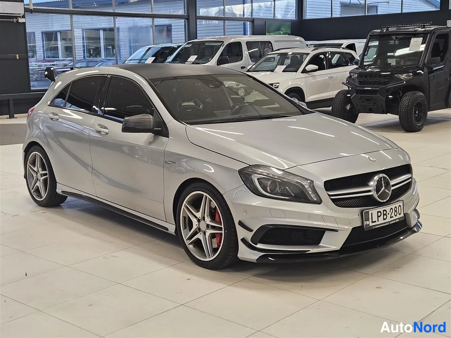 Etuviisto, nokka oikealle: Hopeanvärinen Mercedes-Benz A -mallinen viisiovinen hatchback etukulmasta oikealta kuvattuna autotallissa, rekisterikilpi, AMG-vanteet ja punaiset jarrus