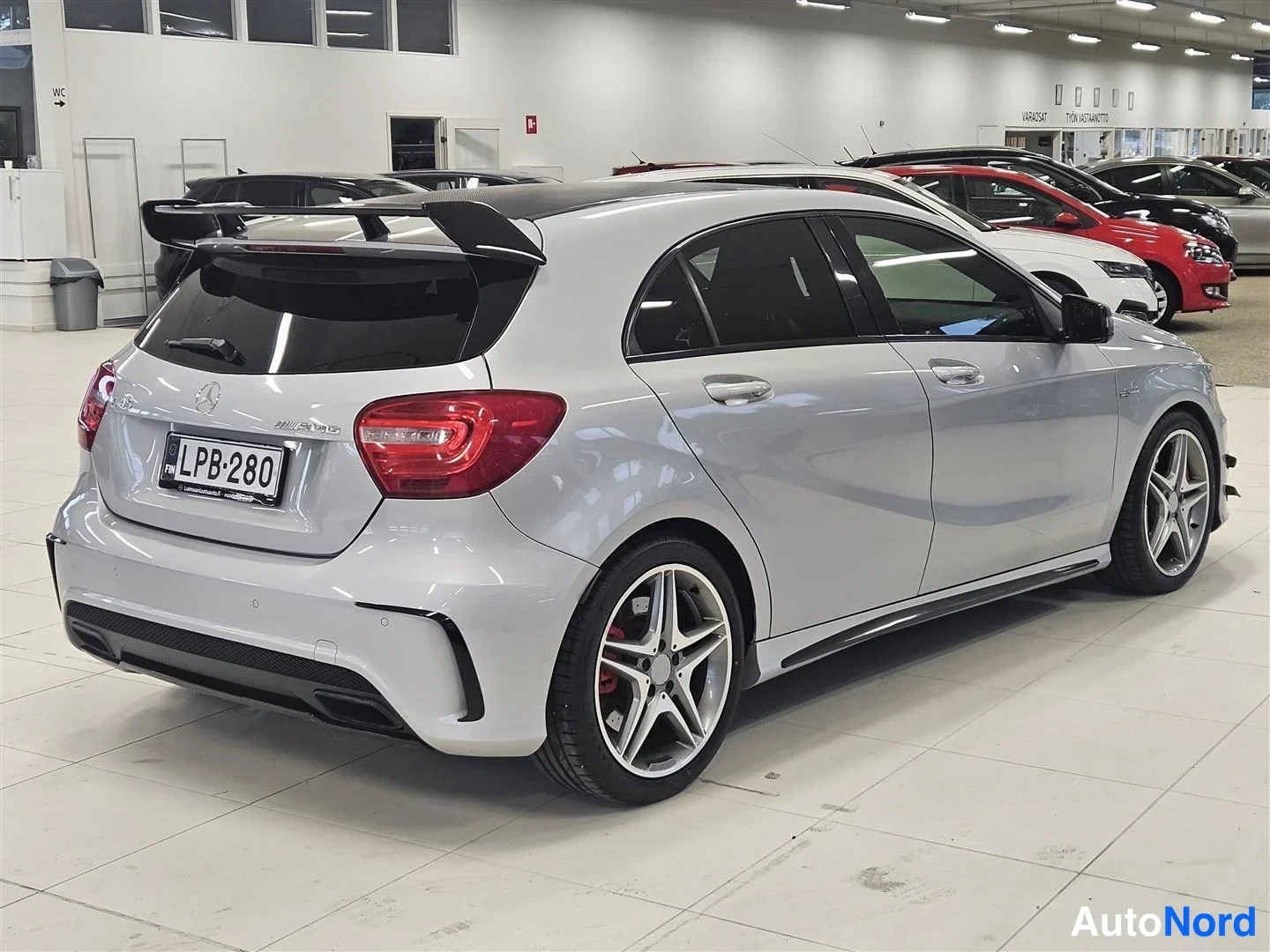 Takaviisto: Hopeanvärinen Mercedes-Benz A 45 -henkilöauto takakulmasta autonäyttelyssä, kattospoileri, punaiset takavalot ja punaiset jarrusatulat näkyvät, rekisterikilpi.