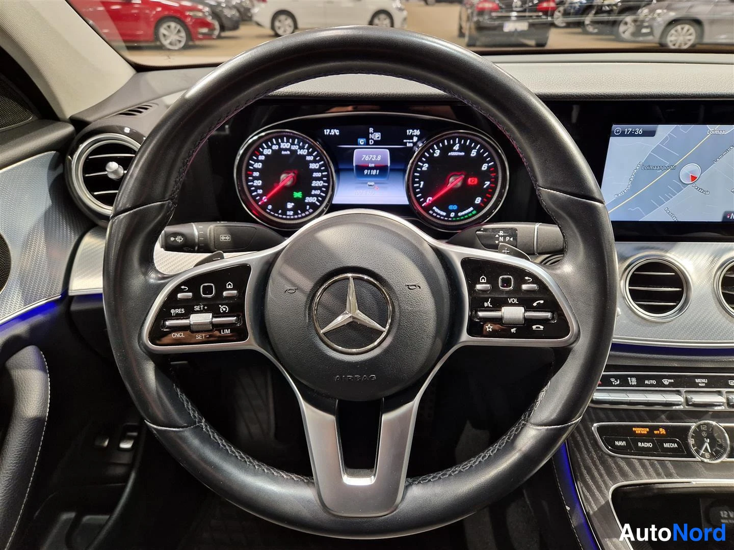Etuviisto: Mercedes-Benzin mittaristo ja ohjauspyörä edestä kuvattuna: näytöllä lukemat 76753 ja 91181 sekä navigointikartta, napit NAVI, RADIO ja MEDIA.