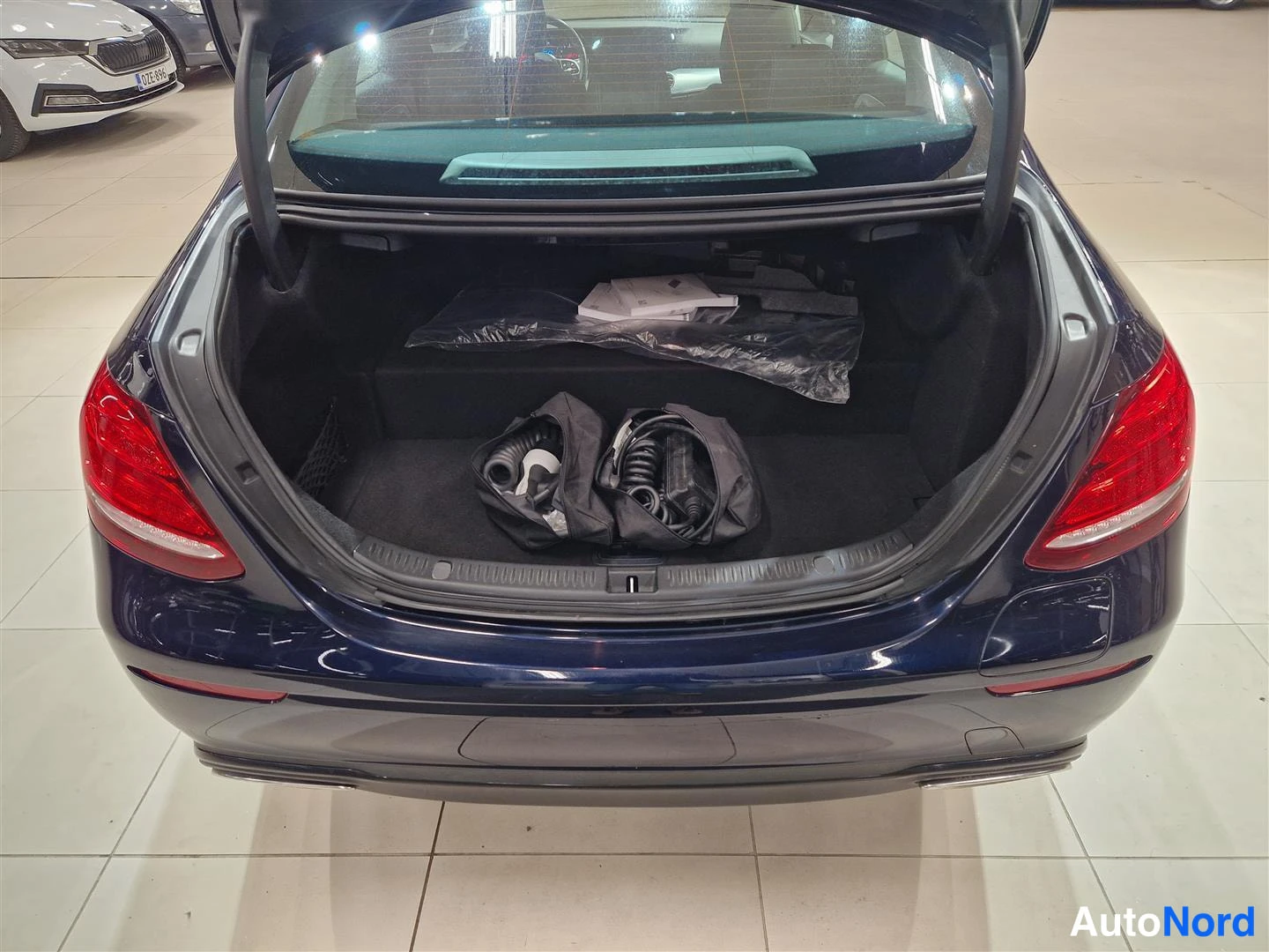 Takaa: Avattu tavaratila takaa: pimeän sininen Mercedes-Benz, musta matto ja laturikaapelit laukussa