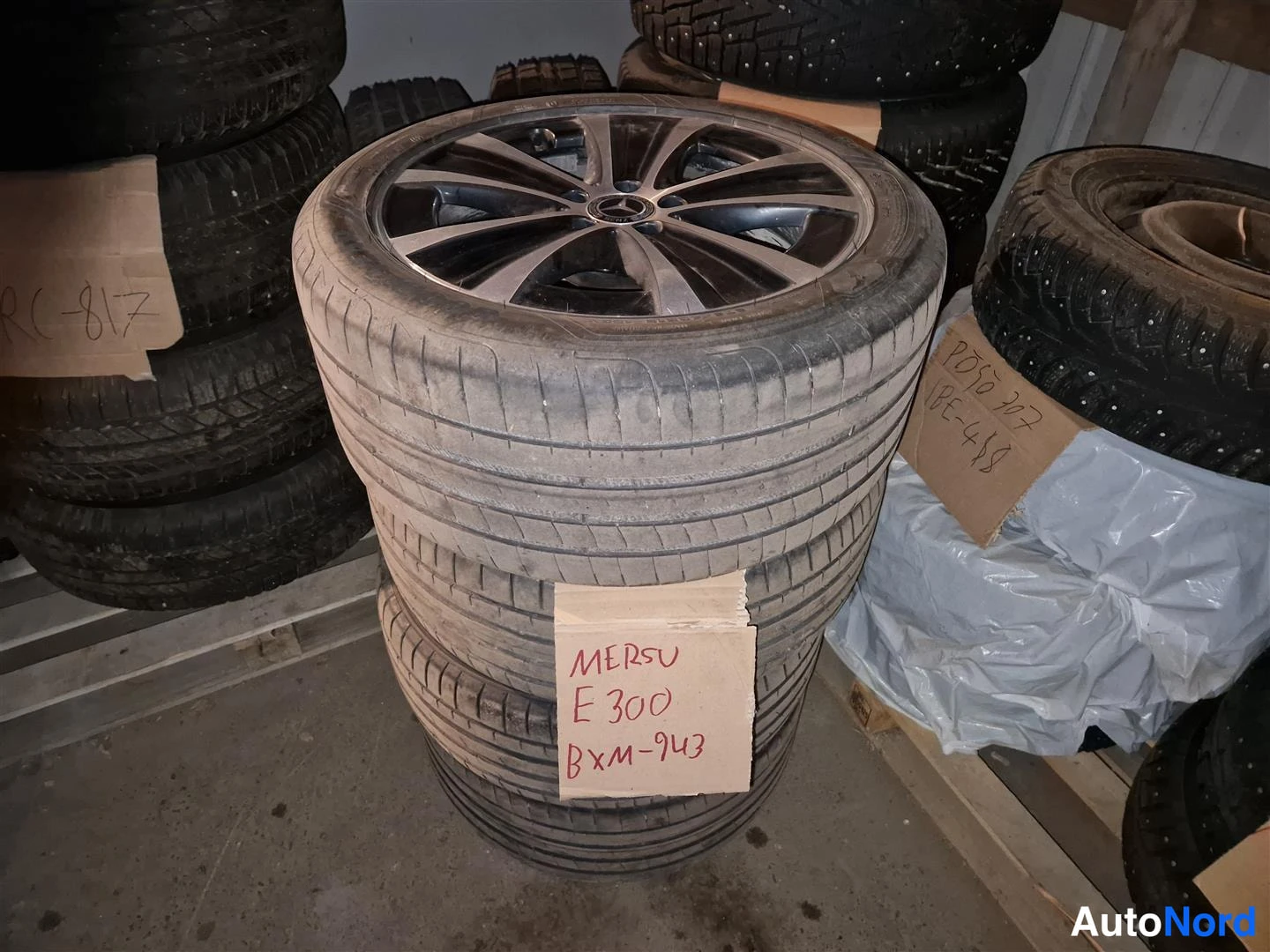Muu: Neliä vanhanlookaista kesärenkaita alumiinivanteilla pinottuna; ylin vanteessa Mercedes-tähtimerkki. Pahvilapussa käsinkirjoitettu teksti MERSU E 300.