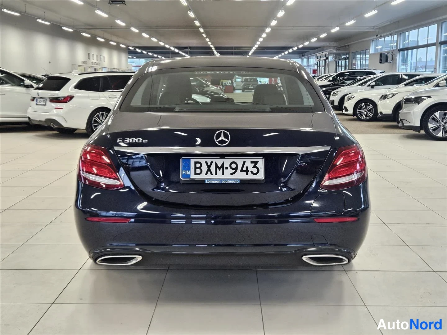 Takaa: Mercedes-Benz E 300e -sedanin takaosa myyntihallissa, rekisteritunnus, kaksoispakoputket ja E 300 e -merkintä