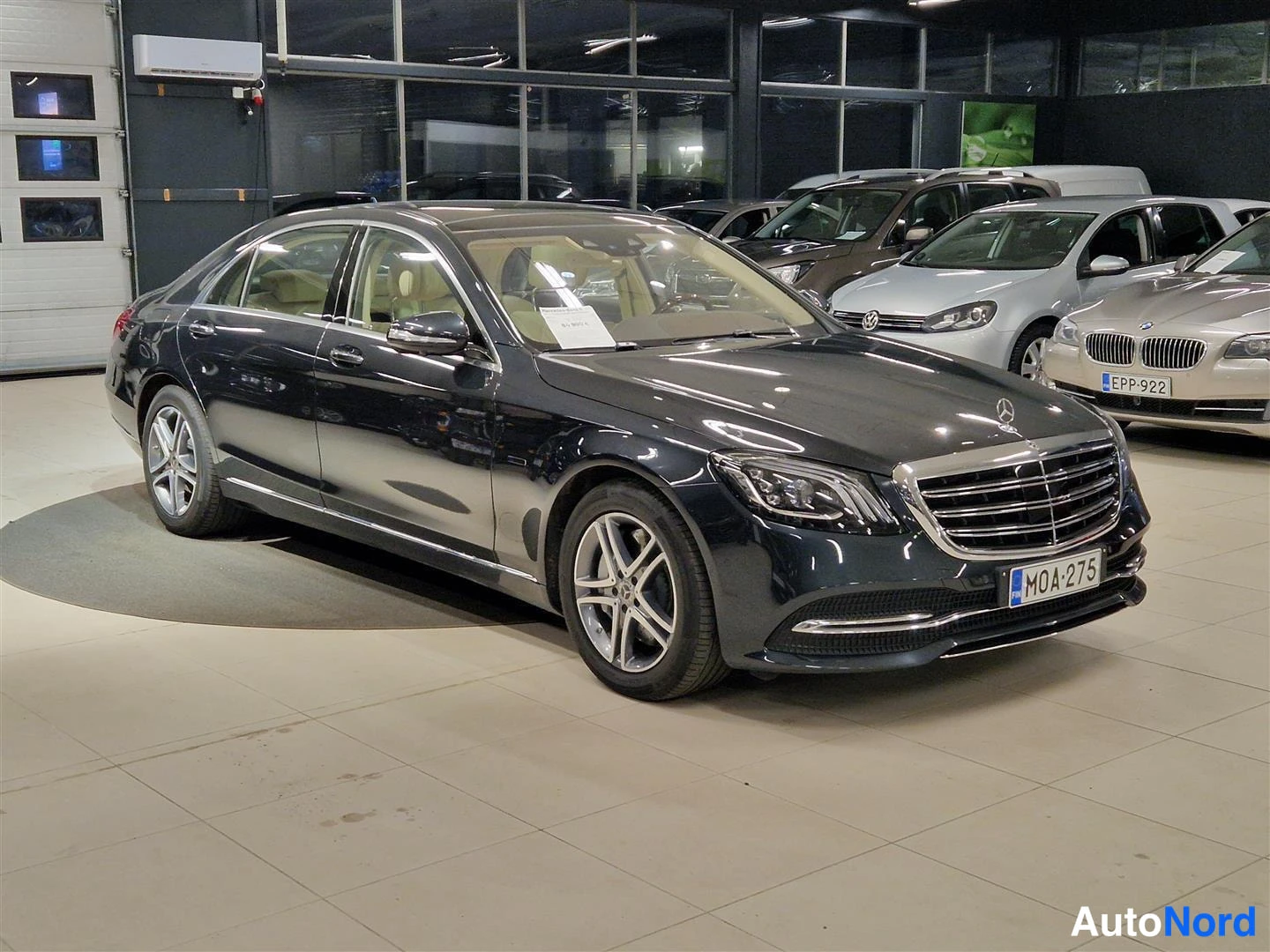 Etuviisto, nokka oikealle: Mercedes-Benz S-luokan sedan tummanharmaana etukulmasta oikealta nähtynä autonäyttelytilassa, rekisteritunnus.