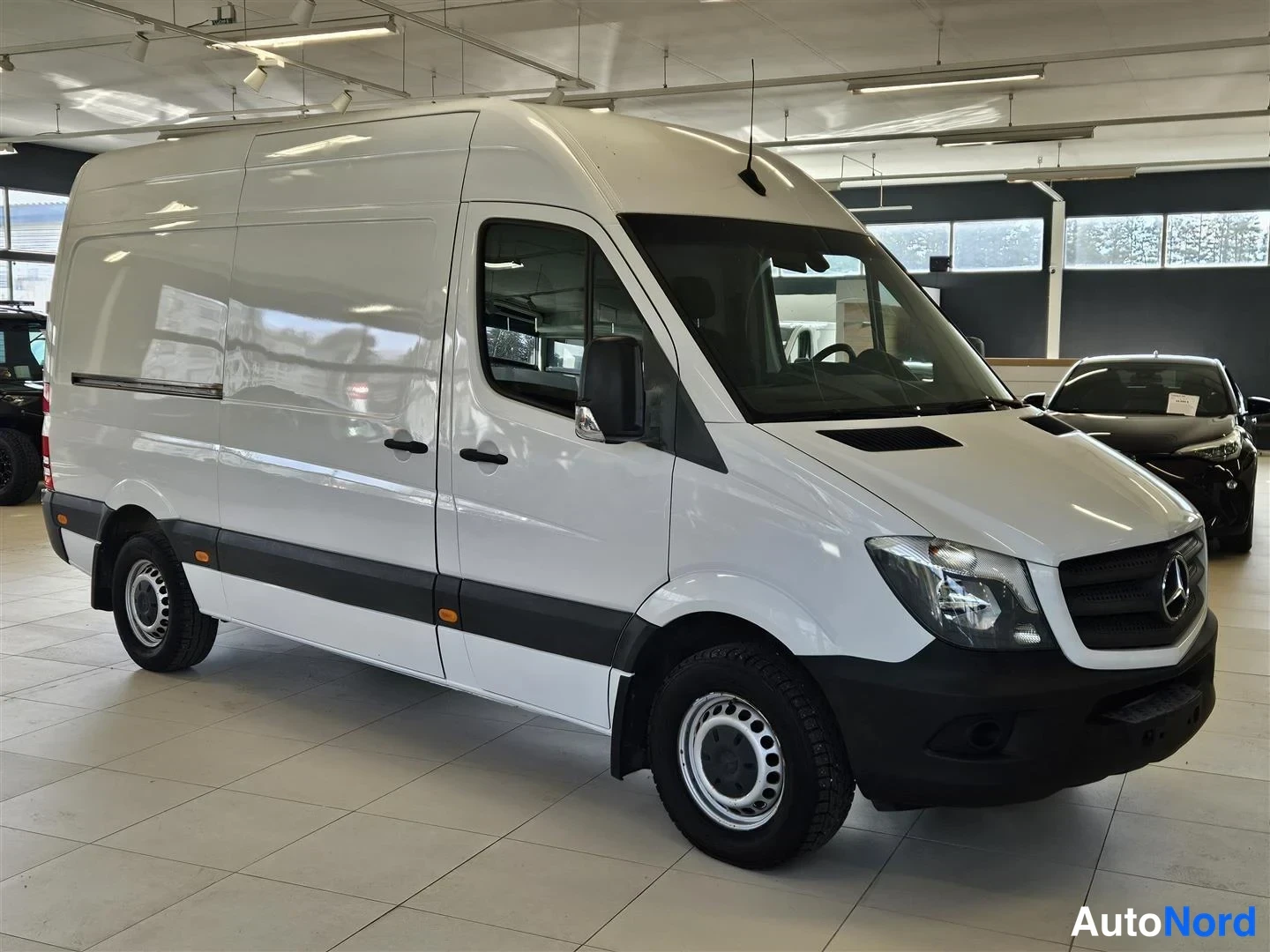 Etuviisto, nokka oikealle: Mercedes-Benz Sprinter -pakettiauto etukulmasta valokuvattuna autonäyttelyssä, valkoinen koripanelointi.
