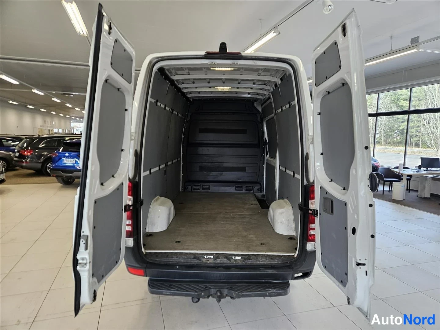 Takaa: Pakettiauton takaluukut auki, autotallin sisällä, kuormatila tyhjä puulattialla.