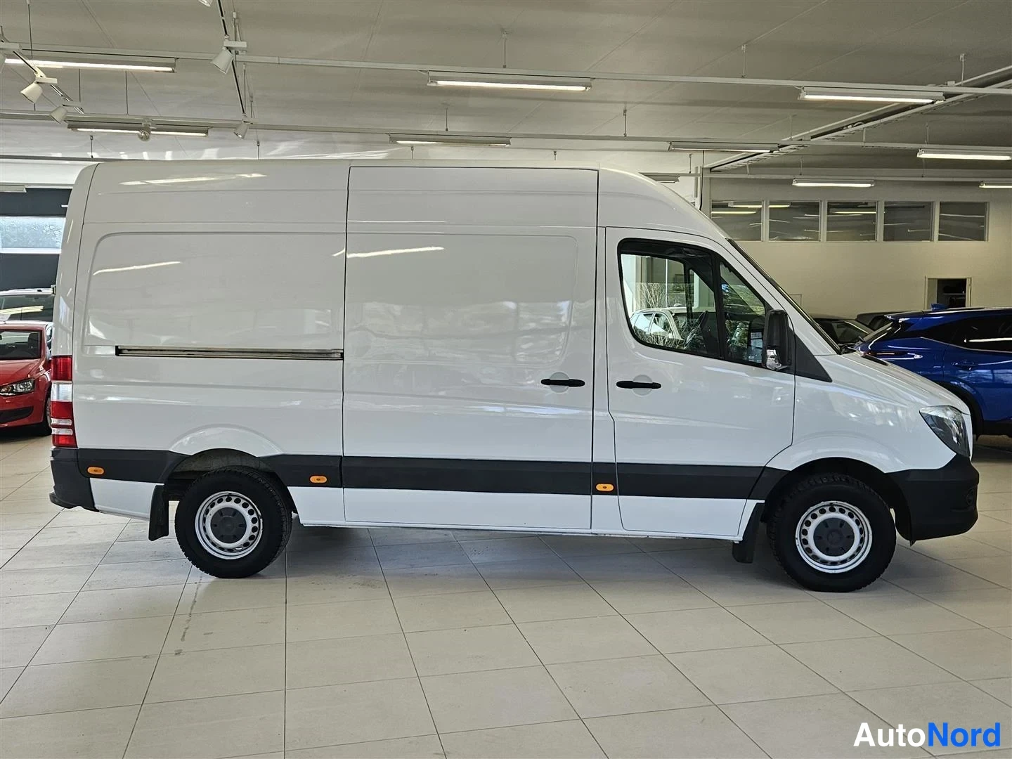 Sivulta: Mercedes-Benz Sprinter -pakettiauto sivulta valokuvattuna autonäyttelyssä, valkoinen koripanelointi.
