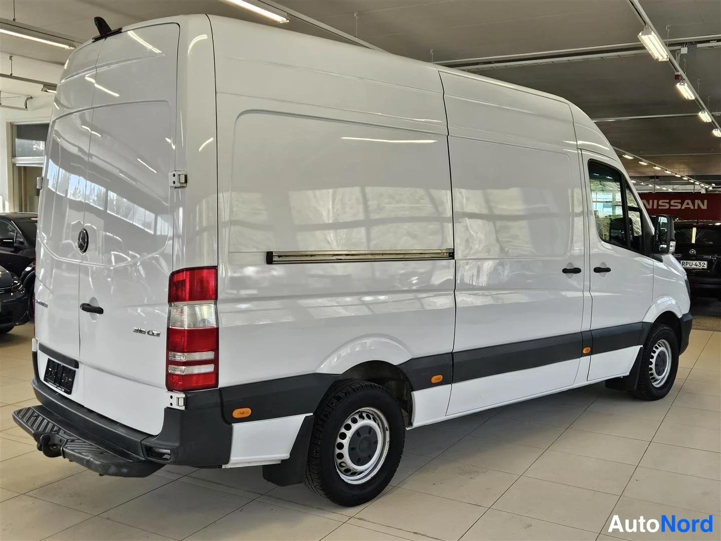 Takaviisto: Mercedes-Benz Sprinter -pakettiauto takakulmasta valokuvattuna autonäyttelyssä, valkoinen koripanelointi.