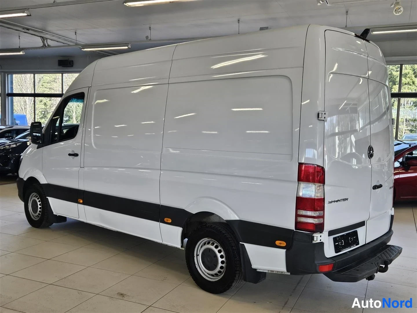 Takaviisto: Takakulmanäkyva valkoinen Mercedes-Benz Sprinter -pakettiauto sisätiloissa, takaa ja oikeaa kylkeä.