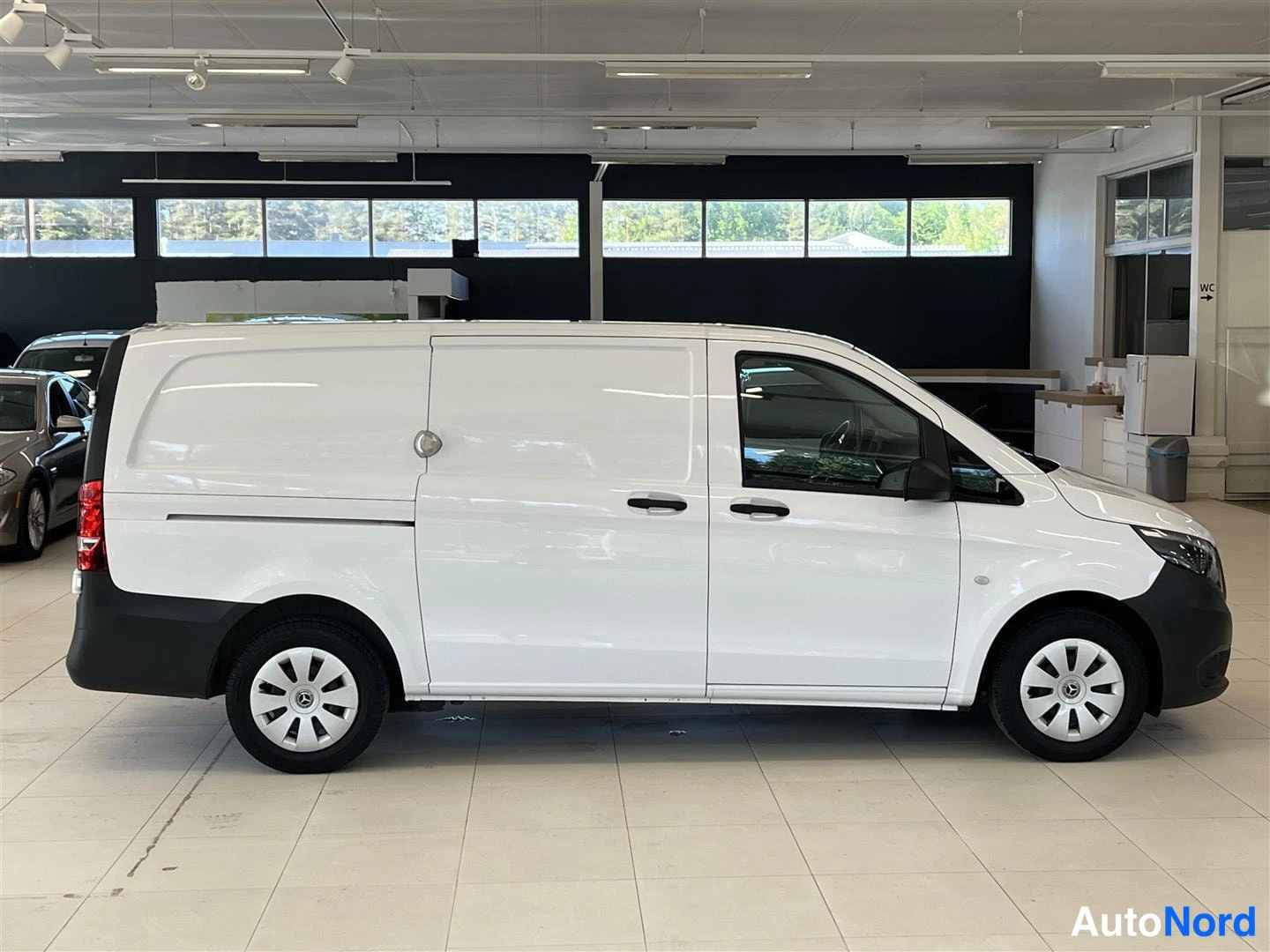 Sivulta: Valkoinen Mercedes-Benz Vito -pakettiauto sivulta nähtynä, auton oikea sivu täysin näkyvissä.