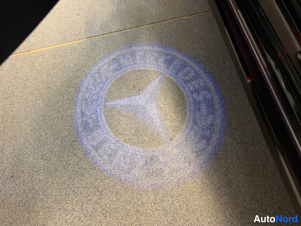 Muu: Avaamaton ovi heijastaa Mercedes-tähtimerkin projektiovalon maahan.