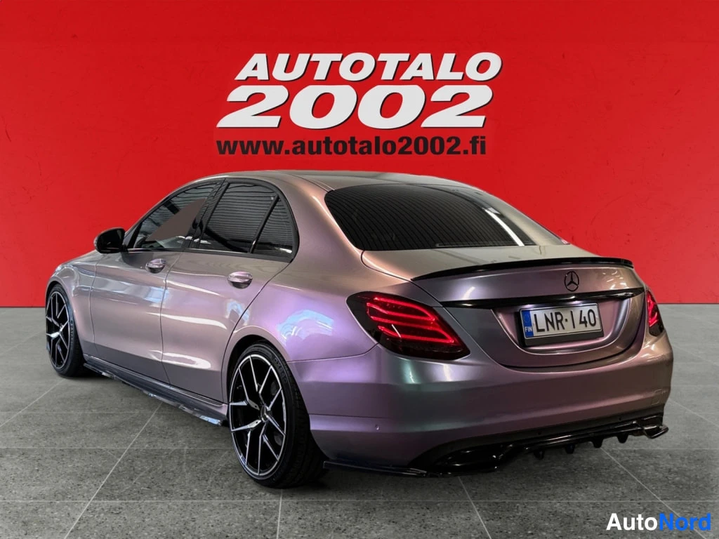 Takaviisto: Autotalo 2002 -taustaa vasten Mercedes-Benz C-sedanin takaostakulma; irisoiva violetti maali, musta spoileri, tuplapakopäätteet ja rekisterikilpi.