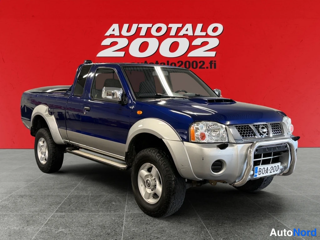 Etuviisto, nokka oikealle: Sininen Nissan NP300 -mallinen avolava-auto etuviistosta oikealta, hopeanväriset levikeharjanteet ja kromikaari edessä, rekisterikilpi BOA·200.